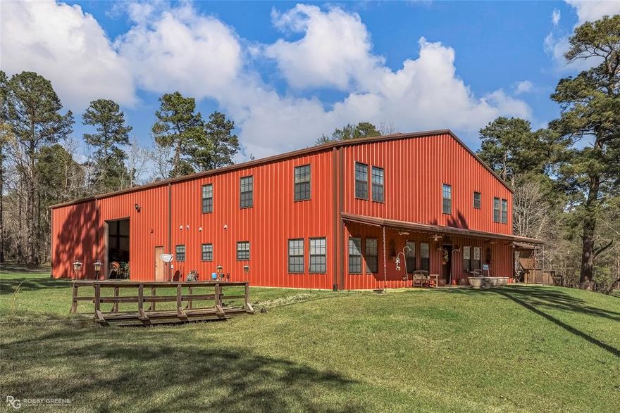 Escape to 26 acres of privacy and versatility with this rare custom-built barndominium offering over 6,000 sq ft under roof and 3,423 sq ft of living space. Designed and built by the owner, a professional builder, this home showcases exceptional craftsmanship, thick insulated walls, and steel construction for long-term durability and energy efficiency. Step inside the two-story residence where spacious rooms and an open-concept living and kitchen area create a warm, welcoming atmosphere. The layout includes three bedrooms, three and a half baths, and a large office easily converted into a fourth bedroom with an ensuite bath. Every detail reflects thoughtful design, from function to flow, making it both beautiful and practical. The shop portion of the barndominium is a dream for hobbyists, collectors, or entrepreneurs. It features three oversized automated garage doors, two built-out workshops or storage rooms, and a mezzanine level with shelving for organization and expansion. Additional structures include a separate RV carport, tractor or equipment shelter, and a detached storage shed. Outside, a large partially covered deck overlooks the fenced acreage with cleared fence lines, offering a blend of open space and privacy. The property is wired for a generator to power essentials during outages, ensuring peace of mind in every season. An added bonus is a secondary homesite with utilities already in place, providing the perfect opportunity to build a guest home, multigenerational residence, or future investment property. Located just outside Blanchard, LA, a growing community with shopping, restaurants, and medical facilities, this property offers the best of both worlds—country living paired with modern convenience. Properties with this space, quality, and flexibility rarely come to market and waiting risks missing the opportunity to own one of Shreveport’s most distinctive homes! Live rural, but never far from everything you need! Space, privacy, and freedom!
