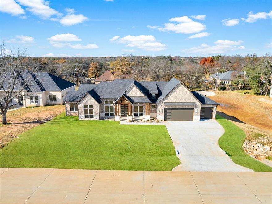 Step into a refined blend of luxury and comfort in this newly built home located within the gated, amenity-filled community of Pecan Plantation. The moment the double front doors open, you're welcomed by soaring 14-foot ceilings, warm engineered wood flooring, and high-end finishes that set an inviting tone throughout the home. The living room offers a beautiful balance of style and function with its custom built-in fireplace and thoughtfully designed cabinetry—an eye-catching centerpiece that enhances the open-concept layout. The adjoining kitchen is built for both everyday living and entertaining, showcasing quartz countertops, a generous gathering island, a six-burner gas cooktop, and stainless steel KitchenAid appliances. A formal dining room and private office greet you off the entry, creating intentional spaces for hosting, working, or unwinding with ease. Your primary suite feels like a peaceful retreat, complete with dual sinks, a free-standing soaking tub, an expansive walk-in shower, and a custom closet that connects directly to the laundry room for ultimate convenience. The split layout ensures privacy, offering a full mother-in-law suite with a walk-in shower and spacious closet on one side of the home, while two additional bedrooms with large closets share a beautifully appointed hall bath on the other. Functional touches continue behind the 3-car garage, where a mud bench, oversized storage closet, and a well-placed half bath add effortless convenience. Outside, enjoy the covered patio which provides the perfect setting for quiet mornings or evening gatherings overlooking the backyard. Built with durability and efficiency in mind, the home includes fully encapsulated spray foam insulation, Low-E windows, and propane gas. Nestled within one of Texas' most desirable master-planned communities, offering golf, dining, parks, and endless recreation right at your fingertips. Experience elevated living in Pecan Plantation.