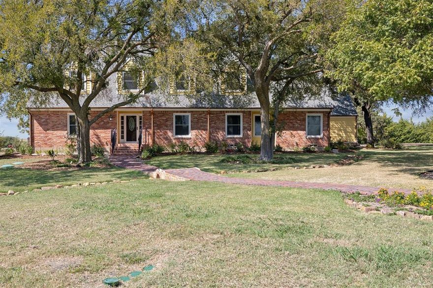 Located in unincorporated Kaufman County with NO HOA, this exceptional farmhouse estate sits on 3.75 elevated acres at over 400 feet above sea level, ideally positioned between Heath, McLendon-Chisholm, and Forney. The loan is a VA assumable at 2.125%!  The setting offers rare privacy, open space, and sweeping long-range views—without sacrificing convenience. Built in 1985 with a level of craftsmanship rarely found today, the home features antique brick sourced from Palmer, Corsicana Cherry Red, Ferris, and Dallas, solid redwood siding, substantial all-wood construction, and oversized structural components. Over the past eight years, the property has undergone extensive, thoughtful renovations with no expense spared, all while preserving its original character. Inside, solid colonial walnut hardwood floors, wool carpeting, custom cabinetry, Baldwin Reserve hardware, upgraded electrical systems, and carefully designed lighting create warmth and quality throughout. The living room is anchored by a working wood-burning stove. The fully renovated kitchen (2018) offers soapstone and quartz countertops, a custom solid walnut island, antique brick flooring, expanded pantry, KitchenAid professional appliances, six-burner gas cooktop supplied by an underground propane tank, double ovens, copper bar sink with Brizo fixtures, reverse-osmosis filtration, and a remotely vented hood system. The private primary suite includes a spa-style bath renovation with heated tile floors, heated towel rack, backlit mirrors, a large walk-in shower with dual heads, quartz countertops, custom cabinetry, and redesigned closets. Outdoors, reclaimed Route 66 antique brick driveway, copper gutters and lighting, flagstone patios, mature landscaping, and open pasture views frame breathtaking Kaufman County sunsets enjoyed from the back porch. Receipts available. A rare opportunity to own a meticulously built and extensively renovated acreage estate with freedom, elevation, and timeless appeal.