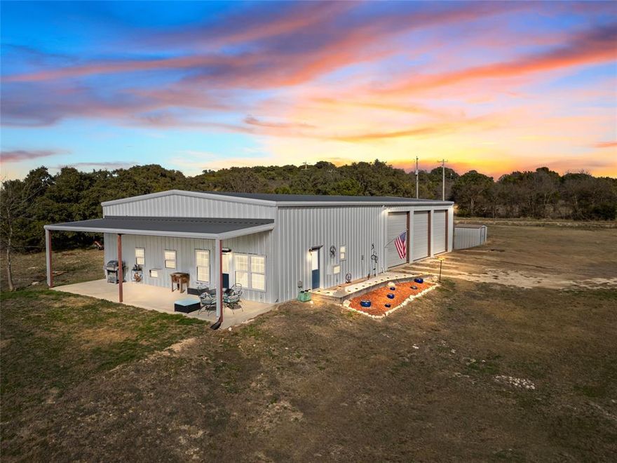 This impressive 3,200 sq. ft barndominium, complemented by a 400 sq. ft. covered porch, offers the perfect blend of modern living and functional workspace.  The fully electric building features a beautifully designed 2-bedroom, 2-bath residence along with a massive workshop- ideal for hobbyists, business owners, or anyone needing space.  The open-concept living and kitchen area is warm and inviting with a large island with bar seating.  The stove, microwave, refrigerator, and bar stools all convey, making this home move-in ready.  A spacious laundry room includes an oversized pantry and convenient access to the shop.  Quality finishes are found throughout, including luxury vinyl plank flooring, stylish light fixtures, and inward-opening windows designed for easy cleaning.  The property is equipped with a private water well and an aerobic septic system.  The shop is a standout feature with three roll-up doors and a half bath.  A car lift and air compressor convey with the property, adding exceptional value.  Situated on rolling terrain with mature oak trees, stunning westward views, the land offers both beauty and privacy.  The property is partially fenced, secluded, and includes a recent survey for added peace of mind.