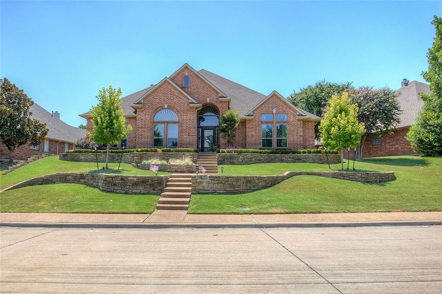 Stunning One-Story Retreat in Desirable Fox Chase! Welcome to this 4-bedroom, 3-bath, 2.5-car garage masterpiece, perfectly situated in the highly sought-after Fox Chase neighborhood—just minutes from The Harbor, the entertainment district, schools, shopping, dining, and convenient access to I-30. From the moment you step inside, you’ll be captivated by hand-scraped hardwood floors, intricate crown molding, and 18-foot ceilings in the foyer with multi-tier lighting that sets the tone for the home’s elegance. The formal living room boasts soaring 15-foot ceilings, while the formal dining room impresses with 12-foot ceilings and granite in all wet areas. The chef’s kitchen is truly the heart of this home, featuring induction cooking, granite countertops, under-cabinet lighting, cabinetry galore, and a large walk-in pantry with a designer glass door. An open-concept floor plan flows seamlessly into the spacious 19x19 family room, where views of the backyard oasis create the perfect blend of indoor and outdoor living.
The primary suite is a private retreat with 18-foot vaulted ceilings, dual closets, a shiplap ceiling, a Barnwood accent wall, and an oversized barn door leading to a spa-like ensuite. Here you’ll find a deep walk-in glass shower with double showerheads for the ultimate relaxation experience. Step outside to your own resort-style backyard—a heated lagoon-like saltwater pool with a cascading waterfall (converted in 2023), lush landscaping, and a shaded patio with a TV and remote-controlled screen. Perfect for entertaining or peaceful evenings. Recent updates include a radiant barrier and new HVAC (2024) for comfort and efficiency, plus the security of a remote-controlled private driveway gate. This home combines luxury, comfort, and convenience in one of Rockwall’s most desirable locations—don’t miss the chance to make it yours!