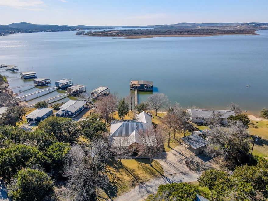 Welcome to a lake home that truly captures why people fall in love with Possum Kingdom Lake. Quality-built lakefront home on a wide, open stretch of Possum Kingdom Lake, located on a quiet, nearly hidden street with convenient access to restaurants, marinas, grocery and hardware stores, and hike-and-bike trails. This property offers good water depth off the dock and a lower boating traffic area, ideal for relaxed lake enjoyment. The open floorplan features high ceilings, a spacious family room connected to the kitchen, granite countertops in kitchen and baths, and built-in surround sound in the living and kitchen areas. Luxury finishes and thoughtful design make this home suitable as a full-time residence, weekend retreat, or short-term rental investment for renters who want a luxury lake experience. The oversized covered rear porch faces prevailing summer breezes and provides expansive water views and stunning sunsets across Palo Pinto lake country. The manicured and irrigated yards includes lush grass, mature cypress trees, landscape lighting, and a shoreline firepit with seating area. Additional features include a brand new metal roof, integrated alarm security system, and generous parking with two covered spaces plus additional concrete parking. The covered dock is designed for functionality and enjoyment, offering a large boat slip with lift, a second boat slip with lift, cable lift for additional storage, PWC lift with stair access that can be lowered to create a controlled-depth play area. Dockside water faucet for rinsing lake gear, and an upper party or tanning deck.  A Pynamite insect misting system services the dock and walkway. This very well-maintained lakefront property combines quality construction, practical amenities, and prime waterfront location.