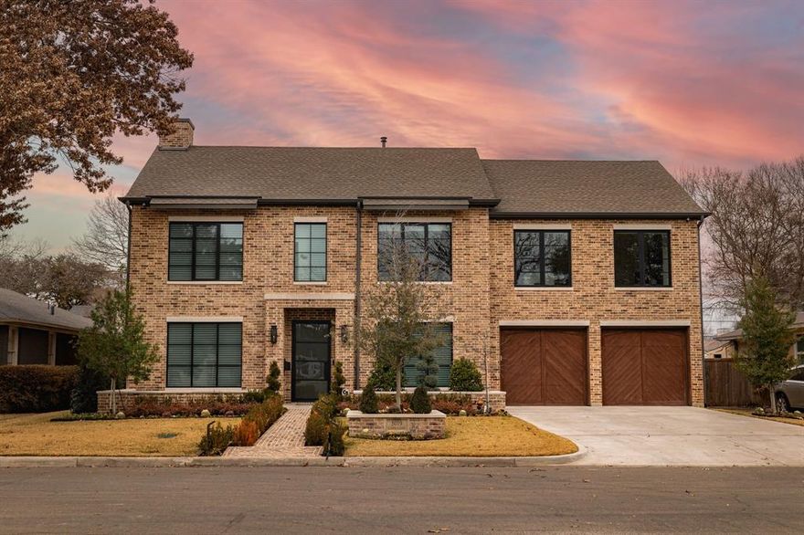 Discover this stunning six-bedroom, five-and-a-half-bath estate on a quarter-acre lot. A timeless brick façade with black steel-frame windows, herringbone wood garage doors, and a brick walkway framed by manicured hedges set the tone for refined curb appeal. Inside, floor-to-ceiling glass floods the open plan with light, highlighting wide-plank white oak floors, designer brass lighting, and custom wall paneling—seen in the chic dining room with a black feature wall and sconces. The great room opens through a wall of multi-slide doors to the backyard and features exposed white oak ceiling beams for warmth and scale. At the center is a chef’s kitchen with a plaster vent hood, built-in refrigerator, natural stone counters and splash, and an oversized white oak island outfitted with dual sinks, twin dishwashers, and a walk-in Butler’s Pantry—ideal for daily living and effortless entertaining. Step outside to a true resort setting: a travertine terrace, covered patio w gas fireplace, ceiling heaters, and retractable shades, plus a built-in stainless outdoor kitchen. The 15,000-gallon heated and cooled pool features a raised spa with spillover and a waterfall. A cedar pergola pavilion provides an additional dining or lounge zone, complemented by a storage shed on slab and a smart 14-zone irrigation system with integrated fertilization. Upstairs and down, restful suites and luxe baths showcase marble surfaces and frameless glass showers; the serene vaulted primary suite includes a paneled feature wall and a spa bath with dual vanities and a makeup station. This home is fully connected: whole-home automation for locks, lighting, and cameras; a Lorex 4K surveillance system; Wi-Fi–enabled appliances with extended warranties; and a 26-kWh natural-gas Generac generator with intelligent load management. Minutes to Downtown Dallas, Park Cities, and Love Field, 5019 Lark Lane blends craftsmanship, technology, and indoor-outdoor living, delivering the best of modern Dallas luxury.
