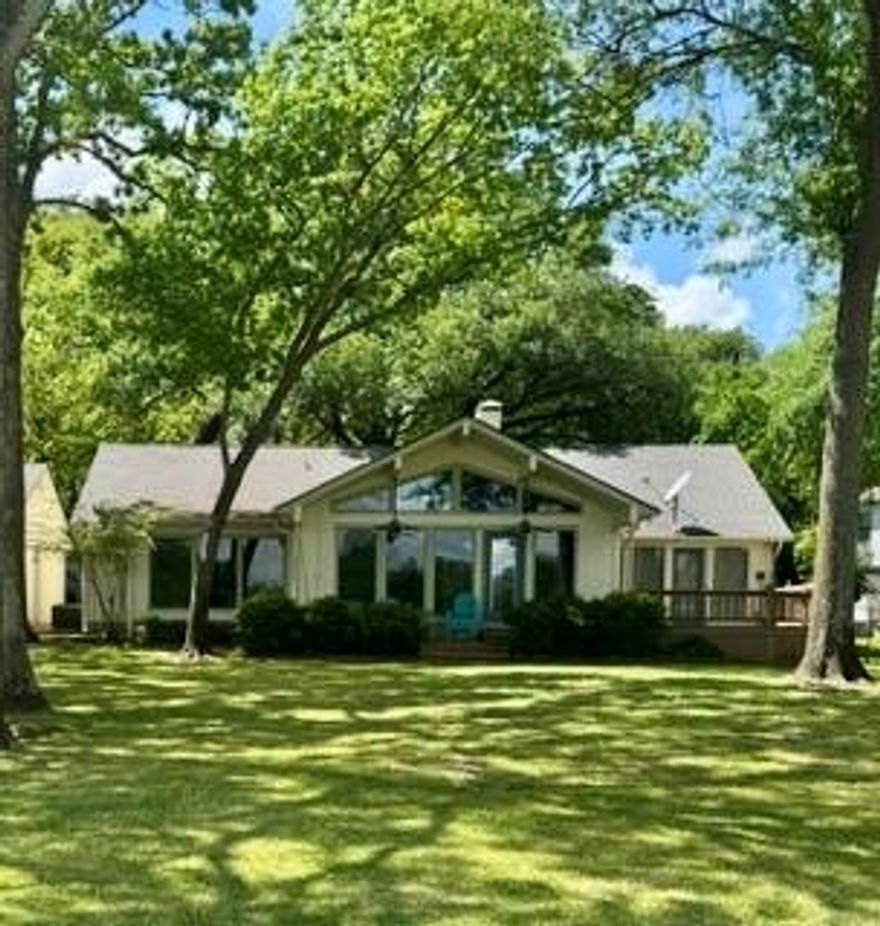 Spacious waterfront home offering two living areas, three bedrooms, and three full baths, plus a two-car garage. The open-concept design features high vaulted ceilings and a brick fireplace creating a warm and expansive feel. A versatile flex room provides the option for a fourth sleeping area, perfect for accommodating guests. Situated on one and a half lots with 158 ft of shoreline, the property showcases a beautiful setting with mature trees and a sweeping views across a large bay. Enjoy outdoor living on the covered porch or separate deck, along with a sandy swimming area perfect for lakeside fun. A private boathouse with sundeck completes this exceptional waterfront retreat.