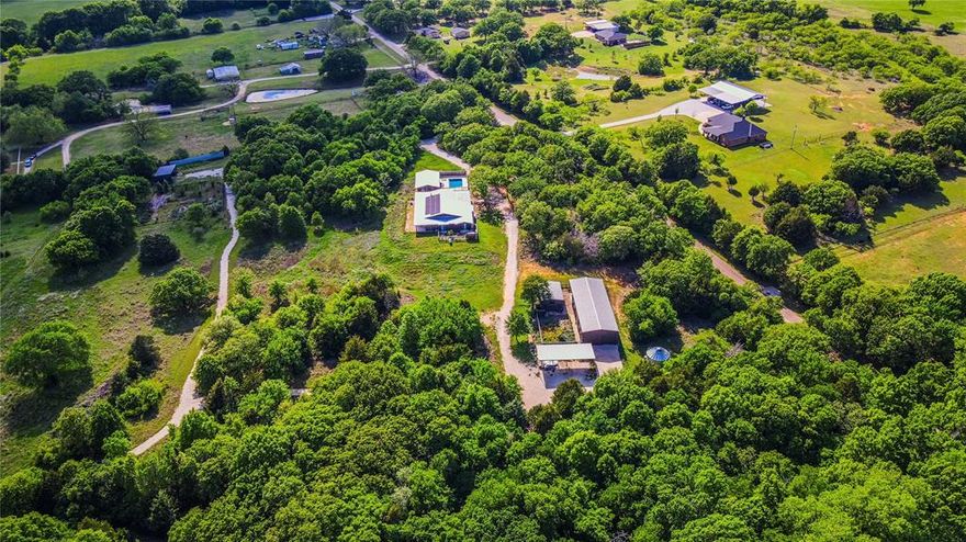 Set on 88 plus acres in the scenic countryside of Grandview, this extraordinary gated estate offers a rare blend of intentional design, natural beauty, and functionality. Built by Ferrier Custom Homes and designed by its owners, this true custom residence seamlessly integrates modern architecture with the surrounding native landscape.  The main home features an open, modern aesthetic with expansive living and dining areas, sleek concrete floors, and walls of glass framing breathtaking views of wildflowers and natural terrain. A stunning fireplace with Motawi tile from Ann Arbor Michigan custom designed by the owner serves as a striking focal point.  The chef designed kitchen is equipped with high end appliances, a European gas range, multiple ovens, oversized island, extensive shelving, and a built in beverage cooler. A spacious utility room and pantry house the solar power system, tankless water heater, washer, dryer, and additional storage.  All three bedrooms offer private baths and access to garden spaces or a large sleeping porch. One secondary bath is constructed as a reinforced saferoom and storm shelter. An additional full bath includes a spa inspired steam shower with wrap around bench seating.  Outdoor amenities include a resort style pool with bath, a one bedroom pool cabana, a putting green, and a turf covered corn hole area or bocce ball court for recreation and entertaining. A large workshop with overhead doors features a barndominium with two bedrooms, one bath, kitchen, and living area. Covered parking for four plus vehicles, along with a hay barn and tractor shed, adds versatility.  The land offers fenced gardens, a Christmas tree farm, gravel drives, and a tree lined creek with abundant wildlife, qualifying for a wildlife exemption. A rainwater recapture system supports the gardens.  Property is fully fenced and gated.  A truly one of a kind property that must be experienced to fully appreciate.