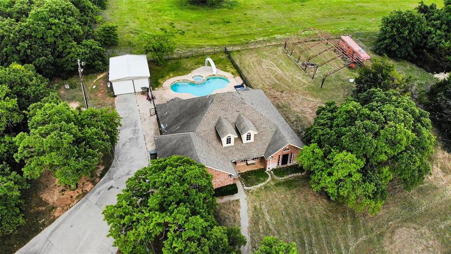 Experience the peace and charm of country living on 3.38 fenced acres with stunning mature trees throughout the property. A long, tree-lined driveway sets the tone as you arrive, offering both beauty and privacy. The 4-bedroom, 2-bath brick home provides a comfortable layout, while the saltwater gunite pool is perfect for relaxing Texas summers. The metal storage building with electricity adds extra space for hobbies or projects. If you’ve been looking for room to spread out and unwind, this one is worth waiting for! The pole barn could be easily finished to house your livestock.