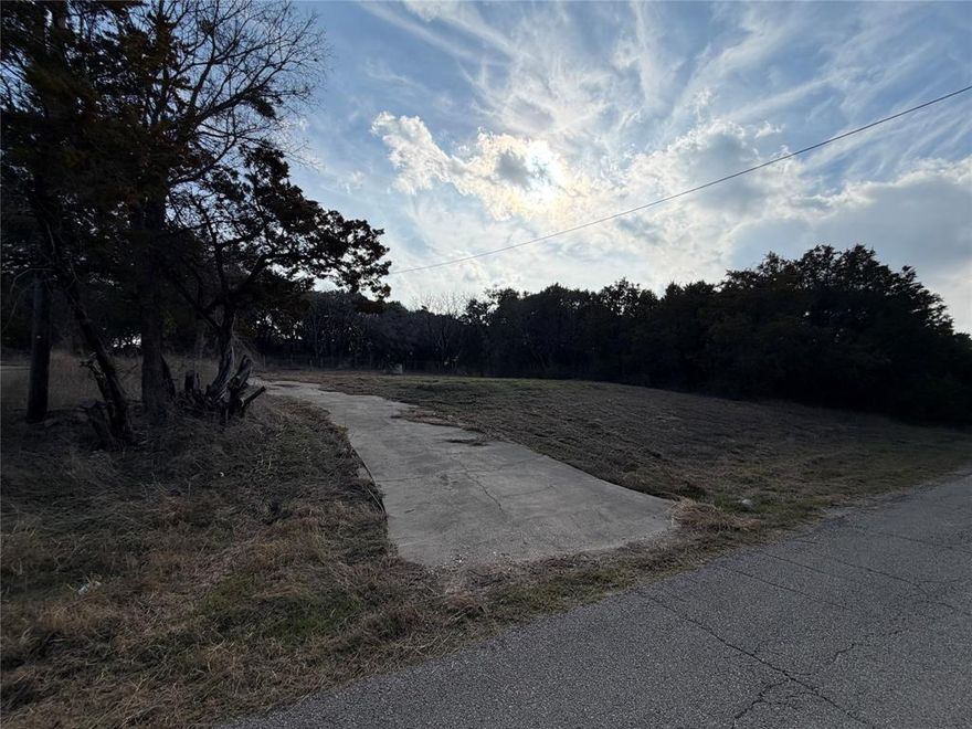 Large, Cleared Lot Ready to Build
Not your average lot. Here is a large, cleared lot ready to build your dream home just a half mile walk down to a community picnic area on Lake Granbury. Rather than the usual 50x100 or 5000 square foot lot, this pie-shaped lot has 95.9 feet of road frontage and is 133.7 feet deep. It is approximately 9630 square feet so it is almost a double lot.
There are already water and electric meters installed on the lot because there was a home on the lot until 2022 when it burned down. The fire debris has since been completely cleared to make the lot ready for building a new home. There is even an existing concrete driveway with a culvert which could be used either to drive to the house or for access to the back yard. The old septic system might not be approved to use for a new build though.
The desirable Comanche Harbor HOA provides good roads, lake access, a boat ramp, fishing areas, and community parks a