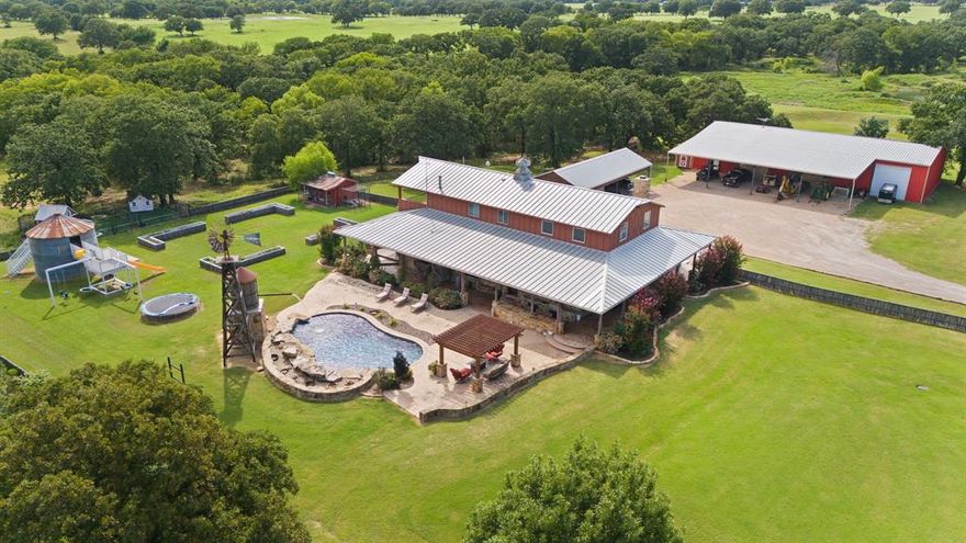 Welcome to a true Texas retreat where rustic charm meets resort-style living. Nestled on expansive, picturesque 30 acres  in the Cleburne, this extraordinary custom estate blends the warmth of a luxury lodge with the convenience and style of modern country living.
From the moment you enter the gated drive, you’ll be captivated by the inviting barn-style architecture with metal roofing and wide wrap-around porches designed for entertaining and relaxation.
Inside, the home is a showcase of craftsmanship and design, boasting soaring wood-paneled ceilings, rich hardwood floors, and hand-selected rustic finishes throughout. The open-concept great room with a dramatic stone fireplace flows seamlessly into the gourmet kitchen, equipped with high-end appliances, custom cabinetry, and a massive granite island perfect for gatherings plus a large walk in pantry and separate formal dining area .  
A beautiful staircase leads to an upstairs loft and primary suite with stone accents , freestanding tub and a closet that is everyones dream .The bedroom opens out to a balcony where you can enjoy your morning coffee while admiring this gorgeous property.  Downstairs there are  spacious bedrooms and spa-inspired baths that provide comfort and style. This home is also nudura insulated and has a room that can serve as a safe room as well.   Whether you’re curling up by the fire, entertaining by the pool, or taking in the panoramic views from your porch, this home delivers an unmatched lifestyle.
 The showstopping backyard features a sparkling, lagoon-style pool complete with rock waterfall, tanning ledge, and elegant landscaping—anchored by a custom windmill feature and stone water tower that adds authentic ranch character. There is also a 50x100 workshop with a 30x80 overhang with 4 large roll up doors plus a man cave upstairs .   Call today to schedule an appointment to see this gorgeous property.
