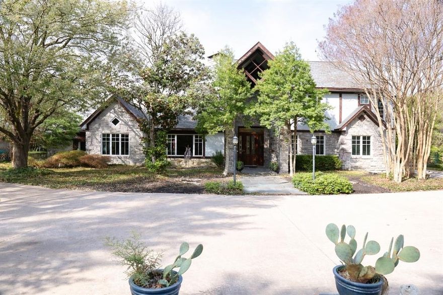 Discreetly nestled on 2.48 private wooded acres in Cedar Hill, this custom 4,000+ sq ft residence offers refined luxury, architectural character, and estate-style privacy. Accessed by a winding drive and framed by stone entry, the home is surrounded by mature trees and serene natural views.
Inside, soaring vaulted ceilings, skylights, rich woodwork, designer built-ins, and wood-framed windows create warmth and architectural distinction. The main level is designed for both entertaining and everyday living, featuring two living areas anchored by stone fireplaces, a formal dining room, and a kitchen with breakfast area overlooking the landscaped grounds and resort-style pool, flowing seamlessly into a wet bar. The primary suite occupies its own private wing and includes a spa-inspired bath with garden tub, separate shower, double vanity, dual walk-in closets, and a distinct adjoining sitting area ideal for lounge, nursery, office, or dressing space. A dedicated home office with adjoining TV room further enhances the flexibility of the main floor. Upstairs, two additional bedrooms and full bath are complemented by a substantial secondary living area with wet bar, creating a private retreat well suited for guests, teens, or multi-generational living. Additional features include a large pantry, spacious laundry room with storage, newer roof, and three AC units. Outdoor living includes a pool, gazebo, expansive patio, and a layered landscape design that frames a defined lawn and gathering areas before transitioning naturally to wooded privacy beyond. Completing the property is a detached three-car garage, separate workshop, and lawn equipment garage. While offering the privacy of an acreage estate, the home remains conveniently positioned near Joe Pool Lake recreation, regional trail systems, major thoroughfares, and access to DFW Airport and the greater Dallas area.