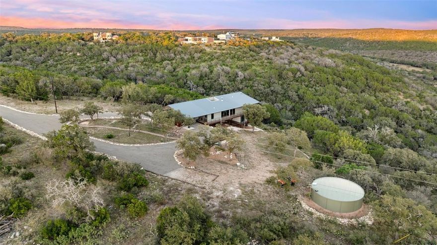 Perched above the rolling hills and limestone outcrops of the gated Wolf Creek Ranch community, this home by LOWDO captures vistas of valleys, trees, and ridgelines near Lake Buchanan. Designed to harmonize with its surroundings, the residence rests on a steel pier-and-beam foundation, minimizing land impact while maximizing views, light, and airflow. A private drive leads through 23.07 acres where free-ranging cattle maintain the property’s Agricultural Exemption. Wildlife is abundant. The home features a 29,000+ -gallon rainwater collection system capturing about 2,510 gallons per inch of rainfall, with a complete filtration system. Built on a south-to-north orientation, it is solar-array ready for future off-grid use. Entry through an exterior “potting room” foyer transitions from outdoors to in. An open-air courtyard floods the interior with natural light and breezes. The main level includes Reform Cabinets from Denmark, engineered wood flooring, and a slider window to a bar and carport area. Sliders on nearly every wall open to wraparound porches (1750 sqft of covered porches) with panoramic views. The living area features a STUV fireplace. Constructed with foam-insulated walls and ceilings, 2x6 framing, red iron beams, and exterior NickelGap siding, Galvalume silver, corrugated steel, and Corten steel with perforated Galvalume detailing. There is a separate entry for the bottom floor. Enjoy sunsets, misty mornings, the Lake Buchanan HOA dock, ATV access to cliffs with easement to Morgan Creek, and the East Lake Buchanan Boat Ramp five minutes away. Designed for sustainability, this Wolf Creek Ranch retreat offers elevated Hill Country living in balance with nature