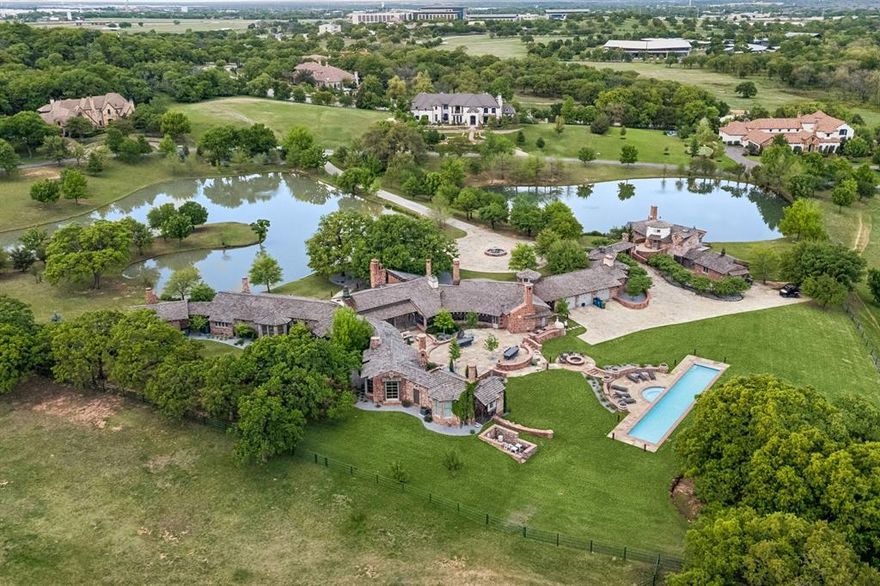 A rare and extraordinary historic estate in the heart of Westlake, this one-of-a-kind 15,000+ square foot residence blends timeless architecture with modern luxury on approximately 16.5 picturesque acres. Originally built in the 1930s by renowned architect Charles Dilbeck for Dallas Morning News publisher Ted Dealey, the home showcases distinctive Tudor and French country influences with reclaimed materials from historic Texas landmarks. Meticulously restored and relocated, the home retains its original character while incorporating thoughtful updates for contemporary living. The main house offers a sprawling floor plan with multiple living areas, a library, private office, and 9 unique fireplaces, each with custom artisan detailing. Architectural highlights include hand-crafted woodwork, rounded walls, turreted elements, stained glass accents, and exposed beams. The chef’s kitchen is equipped with a premium Wolf range, custom cabinetry, and a massive center island. The main house also features a luxurious primary suite, complete with a spa-inspired bath, fireplace, expansive closet space, and serene views. Designed for both entertaining and everyday living, the home includes a finished basement with a home gym, a bonus-craft room, and a temperature-controlled wine cellar with space to entertain, featuring a vaulted brick ceiling. In addition to the main residence, the estate features a versatile lodge house with a striking stone fireplace and wet bar, an ideal setting for hosting gatherings, relaxing with guests, or a dedicated retreat. A separate two-story guesthouse provides additional accommodations with a full kitchen, dining and living spaces, and a bedroom overlooking the peaceful pond. Outdoor amenities are equally exceptional, including a heated pool, three private ponds, rolling hills, mature trees, and abundant wildlife creating a tranquil, resort-like setting. Expansive porches and stone walkways invite you to enjoy the natural beauty of the property.