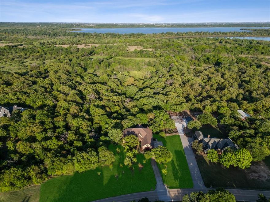 Tucked away in the upscale community of Lakeview Ranch, this custom luxury ranch-style estate is set on a sprawling 1.8-acre lot surrounded by mature trees, gorgeous landscaping & peaceful creek. You'll be wowed when you walk in w-soaring ceilings highlighted by impressive wood beams, HW floors + a stunning floor to ceiling stone FP. Expansive windows frame spectacular views of the wooded lot & outdoor living spaces. Gourmet kitchen featuring a BI smart Dacor refrigerator, custom Alderwood cabinetry, ZLine gas cooktop + Bosch dishwasher. Adjacent to the kitchen is a spacious dining room. The main level also offers 3 bedrooms including the primary suite that provides a private retreat with a spa-inspired bath and dual closets w-a custom dressing room. The super cool lower level is a walk-out basement that is designed for relaxation & entertainment, offering a custom media room w-surround sound, library wall + wine cellar. The Additional rooms provide flexibility for a home office, music studio or hobby space, while the 4th bedroom features a BI desk, sitting area & full bath. The lower level could also be the perfect multi-generational set up! Whole home Wi-Fi + cat 5E wired. Outside, the estate continues to impress w-a resort-style custom patio & full outdoor kitchen featuring granite + stone finishes, a built-in grill, refrigerator, sink + integrated sound. A cozy fire pit & ambient lighting create the perfect setting for gatherings or peaceful evenings surrounded by nature. Enhancing the property’s versatility is a 20x40 workshop, ideal for projects, storage, or additional workspace + an oversized 3.5 car garage. The expansive grounds are maintained w-a private well & irrigation system, keeping your landscaping thriving year-round. With owned solar panels, smart thermostats + integrated lock system, lighting & fan controls, this home blends modern efficiency with a secluded country lifestyle on a large, wooded lot while remaining minutes from Lake Lewisville.