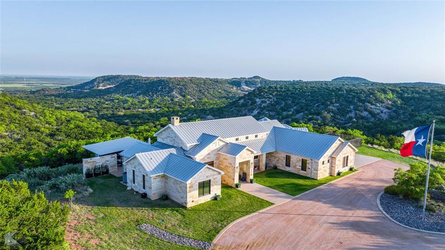 This one-of-a-kind, 3-bedroom, 4-bath home atop Steamboat Mountain outside Buffalo Gap provides unequalled views & interior finishes on this secluded 21.31-acre lot. Situated to showcase the surrounding terrain, oversized plate glass windows and doors flood the home with natural light while framing the stunning vistas and nature’s light show each evening from sunsets over the pool to the west. The primary axis of the home is the 48’ x 22’ open-concept great room, with a substantial limestone block fireplace and living area opposite the kitchen flanking space for a long dining table.  The kitchen has wood beam accents, a massive island with built-in shelving, dual sinks, & stone countertops. High-end stainless appliances, custom cabinetry, a farmhouse sink, & pendant lighting combine functionality with style. Large windows along the west side of the house are shaded by a porch that runs the length of the structure, providing shaded natural light & views that remind the owner: this home cannot be replicated. The 4,908 square foot interior has three HVAC systems (one for the garage with two kennels to keep pets in comparable comfort).  The two secondary bedrooms occupy their own suite & each have ensuite baths. The primary suite has windows that provide expansive views to the north & west, ensuite bath with dual vanities, tub & separate shower with stone finishes. The massive closet hides a built-in safe room for peace of mind. The pool & patio is oriented west, allowing one to enjoy the views to the valley.  A shaded backyard cabana provides additional space to enjoy the outdoors & the views. The standing seam metal roof adds modern durability. The detached 1220 square foot shop is equipped with a commercial HVAC unit & provides ample room for storage, projects, or shelter for up to 4 additional vehicles. The workshop has seller-owned solar panels that provide power to the house & shop for reduced utility bills. More photos at rabbitrun.barnetthill.com.