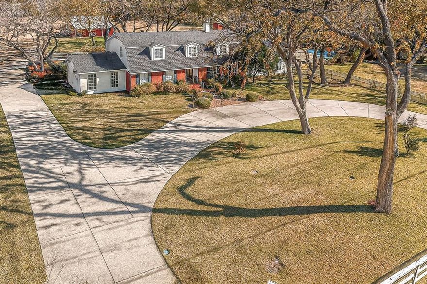 Ranchette in Rowlett ready for your farm animals all on 2.83 acres!  This Gambrel-roof Colonial that’s blended with classic Texas ranch elements with circular drive has a great floorplan for your family including multi-generational.  So much original charm from the 1960’s plus many modern updates. Three ensuite bedrooms with two of them primary suites: one upstairs and one down. The main suite has been completely updated with Spa-like bath featuring a cozy double-sided fireplace next to a deep soaking tub, set against a slate accent wall and matching slate floors. Separate his-and-her closets and dual vanities and with granite counters, plus plenty of storage and getting-ready space. A crystal-style light fixture and charming round window add natural light and a touch of rustic elegance. Secondary suite is perfect for inlaws or teens.  Third bedroom has fun vintage flared bathroom. Warm farmhouse-style kitchen with custom cream cabinetry, glass-front uppers, and vintage-inspired plate rack, all accented by a stacked-stone backsplash and rich granite counters. The wood-planked island with cooktop and striking custom vent hood offers additional prep space, and feels like the heart of the home, perfect for canning days or big family gatherings. Stainless steel appliances.
Throughout this home you will find hardwood floors, beadboard ceilings, recessed lighting, walls of windows bringing the scenic pasture views right in. Discover the oversized rooms throughout with options of dividing spaces up if more rooms are needed. Huge walk in closets in all bedrooms. Study with builtins. Living room features a stone wood burning fireplace and appealing staircase. Family room is spacious, includes a wet bar, and is great for gatherings. 3 full baths, 1 half. Outdoors is just as amazing! The barn has 4 stalls with Dutch doors, office space, room for hay and tack. Swimming pool with rock water feature + stone walkway.  Gardening areas. Pond in the back. Variety of mature trees.