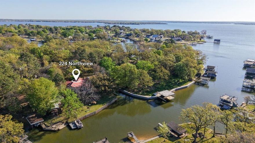 Tucked away on two spacious, beautifully treed lots, this waterfront property offers a rare combination of privacy, character, and potential. With approx. 239’ of platted waterfront and just over three-quarters of an acre, the setting is peaceful and inviting, positioned on a wide cove with a nice view and deep water, plus a newer retaining wall in place.

The home itself is truly one-of-a-kind—full of charm and architectural detail for those who can appreciate design and craftsmanship. While it does need updating, it presents an incredible opportunity for a designer, remodeler, or buyer looking to create a distinctive lake retreat. Interior features include stunning stained glass windows, custom hardwood doors, and brass hardware throughout. The main living area centers around a beautiful stone fireplace with a wet bar, and flows into a sunroom just off the living, dining, and kitchen spaces—ideal for enjoying the tranquil setting year-round.

The split-level layout offers a waterside primary suite upstairs with elevated views of the wide cove, a spacious cedar closet, and a bath with separate tub and shower. Downstairs, a flexible third bedroom includes a Murphy bed and is combined with the utility area, complete with sink and exterior access.

The property is fully fenced with a unique metal and stone entry and private gate, and also features a durable metal roof. A two-car carport and extended driveway provide ample parking.

Located in Trinidad, just minutes from local favorites including Triple N Ranch Winery, Whistle Stop, and the Trinidad Art House, and a short drive to Tool for dining and recreation such as Fig’s Steakhouse and Backyard, and community events at Eight at Tool Park.

An additional opportunity is available with a large, fully fenced double lot across the street (approx half an acre), featuring a two-car garage plus an insulated and sheetrocked workshop—ideal for boat storage, hobbies, or extra parking. Offered separately for $99,000.