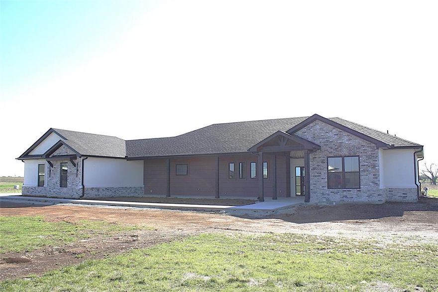 This stunning 4-bedroom, 3.5-bath, 3-car garage home with 2,602 sq ft offers a thoughtfully designed split floor plan and sits on 6.581 peaceful acres in the desirable Willow Moon Ranch subdivision. This property showcases exceptional craftsmanship, energy efficiency, and modern style. Energy efficiency begins with spray foam insulation, making the home extremely efficient year-round. The interior features quartz countertops, custom wood cabinetry, stainless steel appliances including a refrigerator, luxury vinyl plank flooring, ceiling fans in all bedrooms and the living room, and 30-year dimensional shingles. The home also includes a sprinkler system and front and backyard sod. The spacious living and dining area features a stunning beamed cathedral ceiling, abundant natural light, and a multifunction electric fireplace accented with beautiful wood details. The dream kitchen offers generous quartz counter space, double ovens, an abundance of custom cabinetry, a large island, and a breakfast bar with convenient pop-up electrical outlets. Additional highlights include an extra-large pantry with additional storage and workspace, plus a coffee bar with wine cooler. The expansive primary suite features dual vanities, a dedicated make-up nook, a massive walk-in closet, a freestanding soaking tub, and a beautiful tiled walk-in shower. The well-designed laundry room includes custom wood cabinetry, a sink, coat hooks, shoe storage, and quartz countertops for added convenience. One guest bedroom includes a private ensuite bathroom, while the other two bedrooms share a Jack-and-Jill bath, and all bedrooms feature walk-in closets. The oversized three-car garage offers additional storage space. Outdoor living is just as impressive, featuring a large, covered patio with a beautiful wood-burning fireplace and large, covered kitchen complete with a sink. The expansive acreage provides endless possibilities for family recreation, relaxation, and enjoying country living.