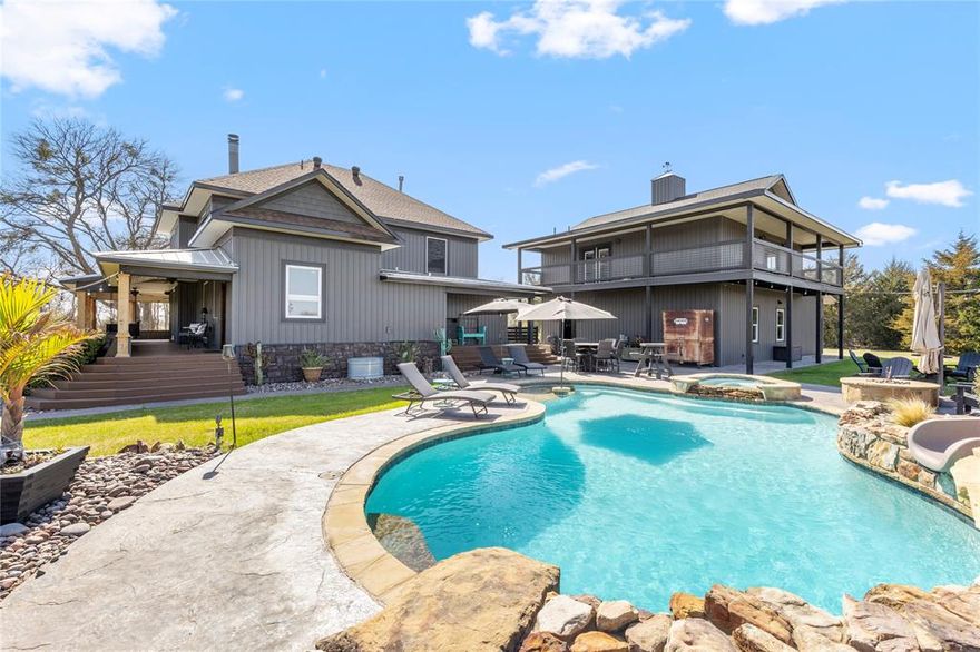 PRICED $25K UNDER RECENT APPRAISED VALUE! Rooted in Hunt County history dating back to 1903, this one-of-a-kind 33-acre AG EXEMPT estate offers privacy, character, and true Texas living. Fully fenced acreage features 4 stocked ponds, a lighted riding arena, holding pen for horses, and abundant wildlife including deer, wild hogs, and mature 8-point bucks, creating a hunter’s dream just minutes from town. Thoughtfully updated while preserving its historic charm, the main home offers 5 bedrooms and 3.5 bathrooms with hardwood floors, an original staircase, cedar closets, custom built-ins, and two double-sided fireplaces. Oversized double-hung windows with solar screens provide efficiency while filling the home with natural light. Upstairs includes Jack-and-Jill suites and a third-story loft ideal for an office or workout space. The primary suite features large windows overlooking the property, a walk-in shower, soaking tub, and separate vanities. The farmhouse kitchen offers granite countertops, abundant cabinetry, and views of the backyard oasis. Outdoor living includes a 9.5-foot heated gunite pool and spa with slide, sun shelf, decking, and firepit. Above the heated 32x32 garage is a 1,024 SF game room with full bath, bar, and balcony overlooking the acreage. A detached in-law or salon suite includes its own bath, plumbing for future expansion, and a separate solar-powered gated entrance. Additional features include an 80x80 shop with lean-to, 60x40 insulated shop with electric and water, RV hookup, updated siding, 2021 roof on house and salon, 2025 garage roof, and 2025 HVAC for salon and garage. The main home has a low-pressure dosage septic system, with a separate aerobic system for the salon. Zoned to A-rated Caddo Mills ISD. Square footage includes game room and salon.