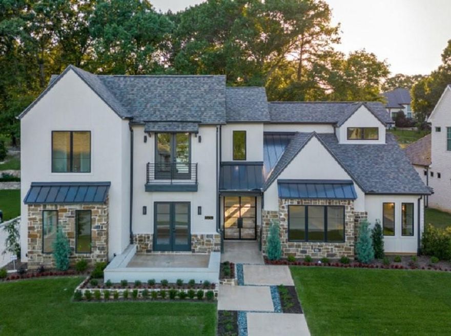 New Construction. Welcome to our stunning Texas Modern home with breathtaking lake views. The elegant tone is set from the first look, with double metal and glass front doors, stone, stucco and brick exterior, and flows inside with remarkable solid cedar interior ceiling beams and headers. The center of the home showcases a luxurious open concept, perfect for gathering and entertaining, with an enormous great room, dining area with wet bar, and striking professional grade kitchen whichshowcases a stunning 11’ long Chantilly quartzite island. The kitchen is flanked by a coffee station, leading to a walk-in pantry, and a separate butler’s pantry - all providing ample storage and seamless convenience for all your culinary needs. You access the motor court and both garages from the kitchen in 2 directions. The primary suite is a serene lake-view retreat with a spa-like bath, perfect for unwinding after a long day, and a room-size closet connected to the laundry room. The large study or den has more lake views through double glass doors that open onto the front terrace for outdoor living or watching the lake in the relaxing pine scented air. Do not miss the attached private cottage suite through the rear entertainment space with outdoor kitchen and fireplace. The comfortable suite or secluded work-from-home office has its own garage access and provides privacy and comfort, making it perfect for extended family members or guests. Upstairs, a central loft opens out to a lake view balcony and three more large bedrooms with their own full bathrooms to provide comfort and privacy for family members or visitors. With its thoughtful design, luxurious features, and stunning lake proximity, this home is tailored to accommodate the needs of multigenerational living while maintaining an atmosphere of elegance and comfort.