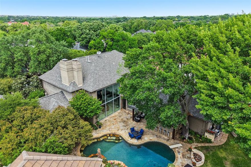 Nestled on an expansive lot in the prestigious guard-gated community of Harbord Oak Estates, this custom Bob Thompson estate offers an exceptional blend of luxury, privacy, and timeless design. Perched beneath a canopy of mature trees, the grand entry makes a striking first impression with stately iron-and-glass double doors. Inside, expansive living spaces are bathed in natural light and adorned with high-end finishes, including floor-to-ceiling windows that frame breathtaking views of the outdoor sanctuary. Designed for both relaxation and entertaining, the backyard showcases lush landscaping with fruiting trees, a PebbleTec heated pool with a waterfall feature, a stone seating area, an outdoor kitchen, and a large grassy lawn—creating a serene retreat that feels worlds away. Indoors, elegance continues with a dramatic room-length bookmatched exotic granite fireplace surround,  soft neutral tones, and warm stone accents anchoring the main living area. The luxurious primary suite is a private haven featuring Venetian plaster walls and a spa-inspired bathroom with custom cabinetry with Blum soft closing hardware, 6cm granite, a walk-in double shower with body sprays, and a Jerusalem stone soaking tub filled from above. A thoughtfully designed custom closet offers extensive built-ins, an island with storage and display lighting. Perfect for hosting, the home includes a central wet bar, wine storage, a secondary living space with an Italian fossil stone fireplace, and a spacious chef’s kitchen. Upstairs, a large game room and spacious ensuite bedrooms provide comfort and privacy for family or guests. Additional highlights include updated window glass (2025), a Class IV impact-resistant roof, a 3-car garage, an in-ground basketball goal, and private trail access leading to White Rock Creek for outdoor enjoyment. Zoned for Plano Schools and ideal location with a convenient drive to downtown Dallas, dining and entertainment.