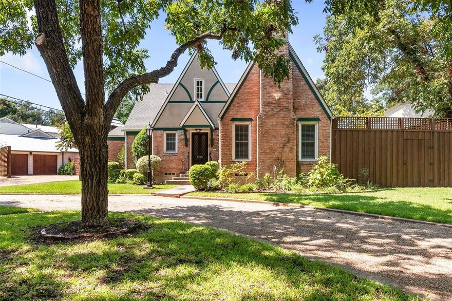 Timeless Tudor-style home with storybook appeal and striking architectural character inspired by medieval English design. The steep gable roof, weeping mortar, decorative half timbering, and tall chimney with ornate brickwork and chimney caps create a dramatic and unforgettable exterior. Leaded glass on the front door and tall, narrow windows invite natural light and enhance the home's charming asymmetry. Inside, cozy spaces with low ceilings and two gas log fireplaces with dentil molding offer warmth and character. Hardwood floors grace the formal areas and main level primary bedroom, adding richness and continuity. The large, updated kitchen is a true centerpiece, featuring a prominent island, granite countertops, marble backsplash, built-in refrigerator and freezer, beverage fridge, central vacuum system, custom cabinetry, and glass-front upper doors. A four-season porch with French doors and its own HVAC system provides a serene space to enjoy year-round. The den includes custom bookshelves, a fireplace, and floor-to-ceiling windows that frame views of the lush surroundings. Upstairs, angled ceilings follow the home’s rooflines, and the updated bath offers a clawfoot tub, vaulted beamed ceiling, separate shower, and dual period-style vanities. The primary bath includes heated floors for added comfort. Outside, a tall iron lamp highlights the home’s natural textures and brick-lined path leading to the front door. An electric gate provides access to the garage with workshop and backyard, where a meandering stone path leads to a private yard. The pie-shaped lot features towering trees, an expansive front lawn, circular driveway, and a more natural, slightly untamed landscape that complements the home’s enchanting aesthetic. Whole house 20 kw generator! Located near Stevens Park Golf Course with easy access to shopping, dining, both airports, and downtown Dallas. This home is a rare blend of historic charm and thoughtful updates in a truly magical setting.