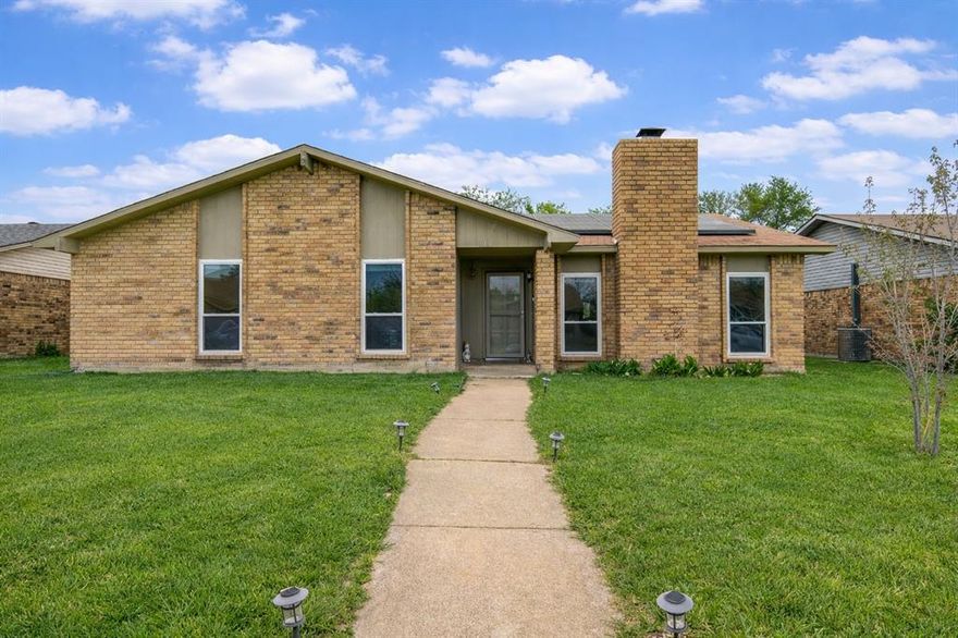 Charming single-story home offering a light located just blocks from Woodhurst Linear Park & Duck Pond Park. Open layout and thoughtful updates throughout with laminate wood flooring that flows seamlessly through the main living areas, complemented by vaulted ceilings and abundant natural light. The inviting living room features a cozy stone fireplace and large windows overlooking the front yard. The kitchen is both functional and welcoming, showcasing painted cabinetry, butcher block-style countertops, stainless steel appliances, and a center island perfect for everyday living and casual dining. Adjacent dining and living spaces create an easy flow for entertaining. The spacious primary suite provides a relaxing retreat with ample room and natural light, while the beautifully updated bathroom features dual sinks, quartz countertops, and a striking walk-in shower with modern tile finishes. Secondary spaces offer flexibility for bedrooms, office, or additional living. Enjoy outdoor living in the private backyard with patio space and plenty of room to play or garden, all enclosed by a wood privacy fence. Additional highlights include a rear-entry garage, auto gate, solar panels for energy efficiency, and a quiet residential setting. Ideally located near parks, shopping, dining, and major commuter routes, this home offers comfort, style, and convenience in one package. Award-winning Coppell ISD.