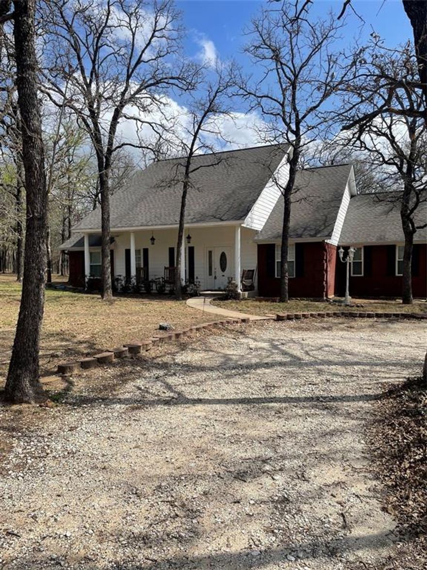 Discover serene, park-like living in this beautifully maintained 3-bedroom 2-bath home featuring a 2-car garage and sweeping views framed by mature post oaks, cedar elm, and hickory trees scattered throughout the grounds. The gated entrance, equipped with solar and electric power, leads to a spacious circular drive offering convenience and curb appeal. New fencing encloses the entire perimeter. Inside, the thoughtfully designed kitchen showcases granite countertops, pull-out drawers, under-cabinet lighting, and abundant storage- perfect for everyday use and entertaining. The split floor plan provides privacy with a generous primary suite featuring a large master bath and his and hers closets. The attic includes a fully insulated, electrically equipped bonus room, providing the perfect climate-controlled storage space. Additional highlights inside include a formal dining room, breakfast nook, large home office and large utility room both equipped with pocket doors, tray ceilings, a plethora of storage, and a striking brick fireplace with a propane starter for wood-burning ease. The backyard features a wooden deck and back porch TV access, ideal for entertaining. A substantial 20x30 workshop, equipped with electric and water, ceiling-mounted air hose reel, and an attached awning, offers an exceptional workspace. Adjacent to the workshop is a freestanding carport to provide additional parking. Toward the rear of the property, you'll find several scenic nature trails, a small gully, and thoughtfully cleared, picnic-style areas that enhance this property's natural charm. Ideally situated just minutes from Lake Whitney, the property offers convenient access to both Waco (approx. 40 min drive) and the Dallas-Fort Worth metroplex (approx. 1 hr drive), placing it in a highly desirable, strategically located area. This property blends comfort, functionality, and natural beauty, ideal for anyone seeking peaceful surroundings without sacrificing modern amenities.