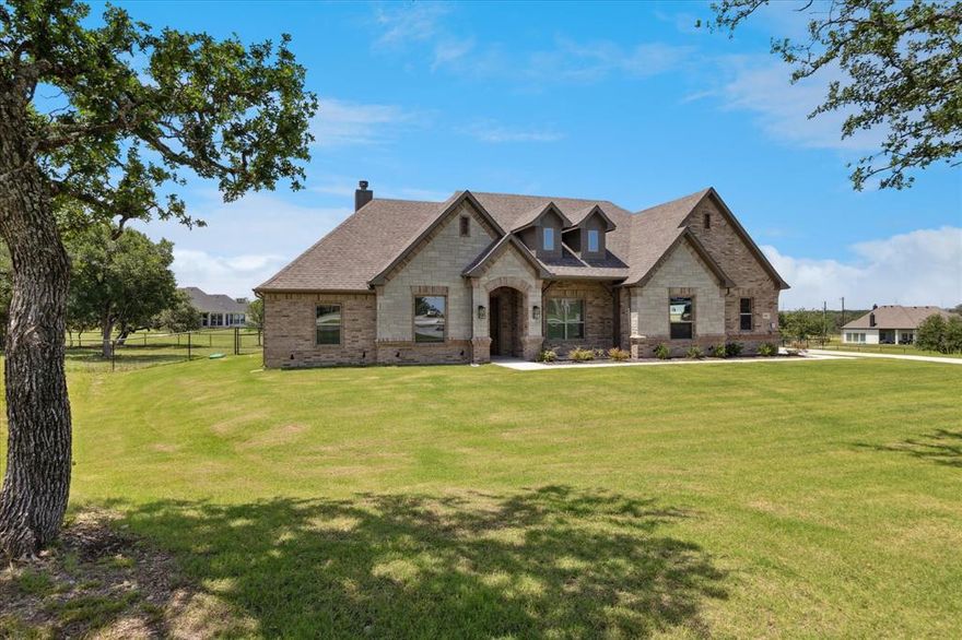 Welcome to 341 Oak Meadow Lane – a custom-built retreat on 1.16 acres in the scenic Vintage Oaks community of Weatherford! This beautifully designed single-story home offers 3,104 square feet of living space with 4 bedrooms, 3 full bathrooms, a dedicated home office, and a spacious upstairs bonus room perfect for a game room, media room, or second living area. Enjoy an open floor plan with high ceilings, abundant natural light, and wood-look tile flooring throughout the main living spaces. The living room features a striking floor-to-ceiling stone fireplace, while the chef’s kitchen boasts a large island with bar seating, quartz countertops, stainless steel appliances, a walk-in pantry with ample storage, and plenty of cabinetry. The primary suite is a true retreat, featuring a luxurious ensuite bath with dual vanities, a soaking tub, separate shower, and direct access to a spacious walk-in closet. All secondary bedrooms are generously sized and include walk-in closets. Step outside to your private backyard oasis complete with a covered patio and outdoor fireplace, ideal for entertaining or relaxing year-round. The entire backyard is enclosed with a custom piped fence, perfect for pets, play, and added peace of mind. Other highlights include a 3-car garage, energy-efficient construction and located in Azle ISD. This home offers the perfect blend of space, function, and country charm — all in a quiet neighborhood setting just outside of town.