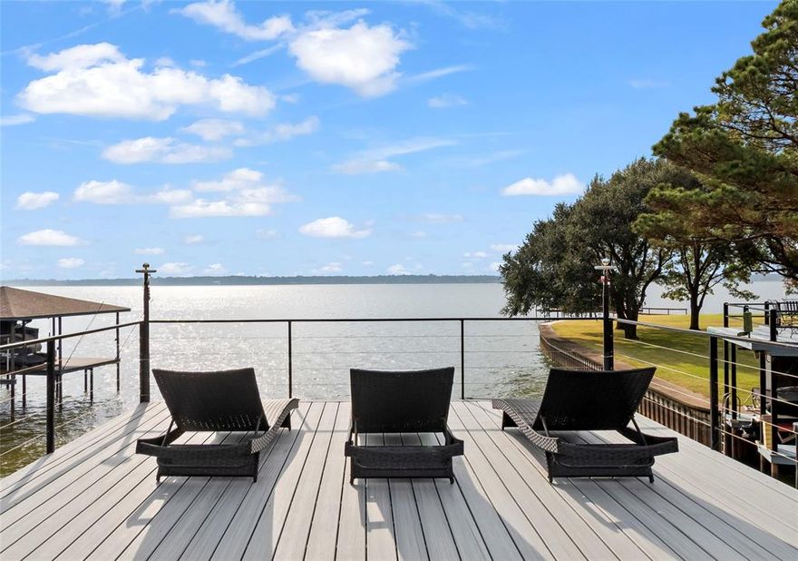 Stunningly renovated waterfront 2,920 sq ft home in Gun Barrel City on Cedar Creek Lake offering 4 bedrooms, 3 bathrooms, an oversized 2-car garage and open-water views. The spacious living room features large picture windows and a striking Austin-stone fireplace flowing into two dining spaces—a dedicated dining room (perfect place for combination dining game table) and a breakfast area. Connected to both dining areas, the open kitchen includes newer black stainless appliances with a convection oven and flat cooktop, a walk-in pantry,  island, and  bar seating for. Tall ceilings,  LVP flooring, decorative lighting, and a clean designer feel extend throughout. The waterside primary bedroom on the main floor features deck access, picture windows capturing open-water views, and electric blinds. The ensuite bath features a dual-sink vanity, walk-in shower with glass surround, soaking tub, and two walk-in closets. A second downstairs bedroom with full bath great for guests or full time living. Upstairs, an extra-large waterside bedroom includes a private waterside balcony, while another bedroom offers built-in bunks (two queens down, two twins up) and a walk-in closet. A full bath with a tub-shower combo serves both rooms. Outdoor living shines with a covered patio and extended deck with multiple seating areas, a hot tub, and a wrought-iron fenced yard that extends beyond the fence and includes a flagstone fire pit area. The boathouse features composite decking, modern railing, a party deck, lighting, and a cradle for a wake boat. Lake stairs allow easy water access, and a lake-pump sprinkler system. A large concrete driveway provides ample parking plus a two-car garage. Located in a desirable site-built community, the neighborhood includes a gated park with a boat launch, pavilion, and fishing pier, with easy access to Gun Barrel City shopping and dining. Short term rentals allowed with permit from Gun Barrel City. Furnishings and Watercraft available separately.