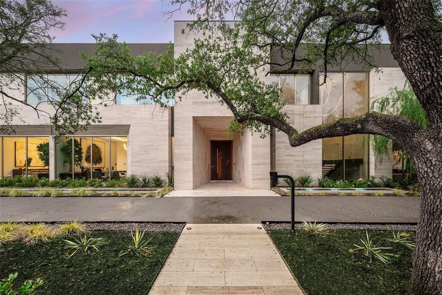 Set on iconic Strait Lane, 10920 is a contemporary estate designed to feel like a private resort—offering 11,211 square feet on approximately 0.72 acres in prestigious Preston Hollow. Behind dual gates, the home makes an immediate impression with clean architectural lines, soaring ceilings, and walls of custom windows that flood the interiors with natural light while seamlessly connecting to the outdoors. Timeless materials and thoughtful design define the residence. Ojinaga limestone and Travertino Jalapa accent walls bring warmth and texture, while white oak millwork carries throughout—from bespoke cabinetry to meticulously finished closets. The open-concept chef’s kitchen is ideal for entertaining, featuring premium appliances, expansive prep space, and a dedicated wine room for effortless hosting. Visual Comfort lighting and statement chandeliers create an elevated ambiance from day to night. The main-level primary suite serves as a private retreat, complete with a spa-inspired bath featuring enclosed dual showers and a spacious custom closet with a center island. A variety of living spaces include formal dining, a sunlit living room with bar, a private office with built-ins, media and game rooms, and a main-floor guest or staff ensuite. Dual utility rooms—one on each level—add convenience.
Outdoors, a covered loggia, full outdoor kitchen, pool, and firepit are surrounded by mature trees, curated landscaping, and ambient lighting, creating a secluded backyard oasis. A five-car garage and private balconies complete this exceptional offering on one of Dallas’s most distinguished addresses.