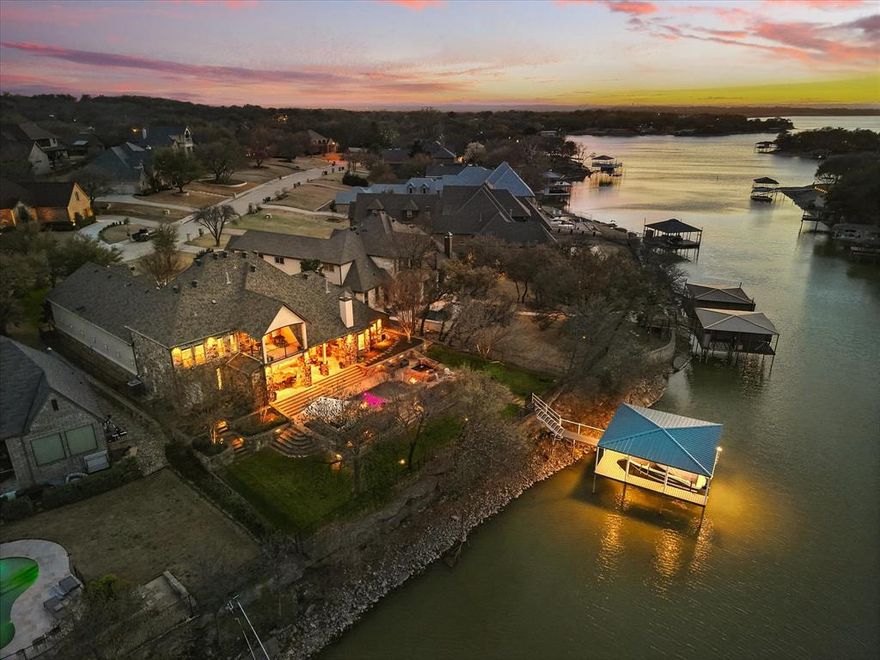 Experience lakeside living in this stunning executive home on Eagle Mountain Lake, nestled in the gated community of Waterfront Addition. This exceptional property features a structured boat dock designed to accommodate all your water toys, plus a lovely sitting area to enjoy breathtaking sunsets. Designed for both relaxation and entertainment, the outdoor living space is a true showstopper, complete with a cozy fireplace and sitting area, an adjacent dining area with a built-in grill, and a refreshing pool showcasing mesmerizing fire and water features or unwind in the Texas-sized hot tub. Step inside to discover a beautifully updated kitchen with chef-quality appliances, including a Monogram 4-burner gas range with griddle, multiple ovens, a convection oven-microwave, and a warming drawer. The enlarged dining room is designed for large gatherings, ensuring you have plenty of space to entertain in style. The spacious family room is the heart of the home, featuring a wall of windows that frame the outdoor entertaining areas and the tranquil cove beyond. The primary suite is on the main level with a peaceful sitting area, a spacious spa-like bath, and a dream-sized closet. Three additional bedrooms up each with ensuite baths ensure comfort and privacy for all. Upstairs, a beautiful wet bar with custom cabinetry and beverage refrigerator with an ice maker seamlessly connects to the large media room. The game room offers even more space for fun and relaxation and opens to a balcony with stunning lake views. For the car enthusiast, the dream garage provides space for six vehicles, along with additional storage for pool and boat toys. A private electronic gate encloses the large courtyard, adding an extra layer of security and exclusivity to this magnificent retreat. This is more than a home—it’s a lakeside sanctuary designed for those who appreciate the best in waterfront living. Don't miss the opportunity to make this exquisite Eagle Mountain Lake estate yours!