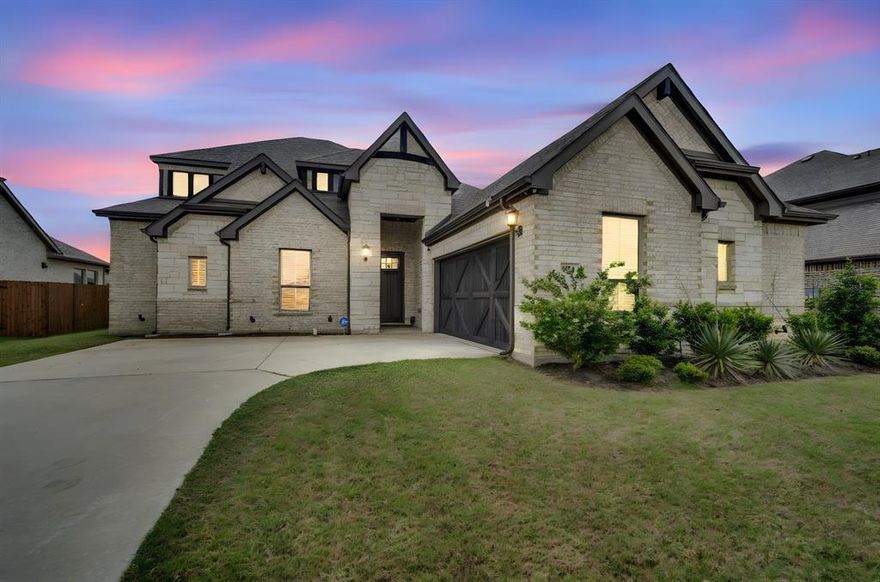 Stunning Tudor-inspired home featuring crisp limestone exterior, dramatic dark trim, and charming barn-style garage door with exceptional curb appeal. Step inside to a grand foyer with tray ceiling and engineered hardwood floors flowing throughout the open-concept main living area. The chef's kitchen impresses with floor-to-ceiling white cabinetry, quartz island with seating, gray subway tile backsplash, stainless appliances, and a dedicated coffee-butler's bar. The expansive living room opens seamlessly to the kitchen and dining area — perfect for entertaining. Retreat to the spa-like primary bath boasting dual vanities, soaking tub and separate walk-in shower. With high ceilings, abundant natural light, and designer finishes throughout, this gem blends modern farmhouse elegance with everyday comfort. The generously sized lot offers endless outdoor possibilities — plenty of room to add a resort-style pool, playground, or open space for kids and pets to roam freely. Schedule your private showing today — homes like this don't last long!