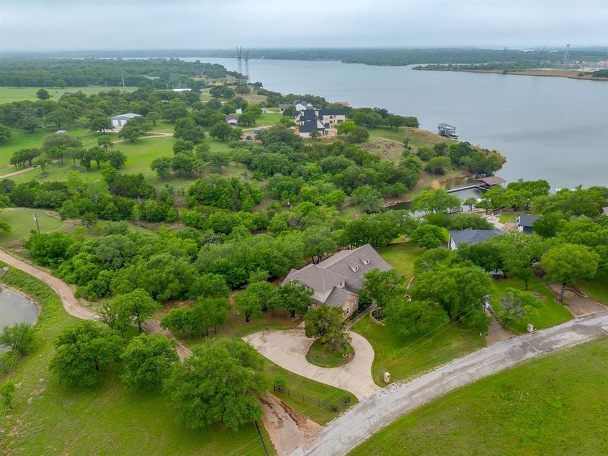Set on a quiet, private stretch of waterfront on the Fort Worth side of Lake Granbury, this rare custom home offers the ideal balance of seclusion, accessibility, and a beautiful view of the lake. Positioned in a protected cove with a clear sightline to the main body of water, the property delivers both calm shoreline living and scenic water vistas. Built in 2012 by Couto Homes, this fully custom 4-bedroom, 3-bath home was thoughtfully designed with oversized walkways and doorways to provide ease of movement and wheelchair accessibility throughout. The open-concept floor plan is anchored by expansive floor-to-ceiling windows that frame the lake, filling the home with natural light and uninterrupted views. The main living area features a gas fireplace and flows seamlessly into the kitchen and dining spaces, creating an ideal setup for both everyday living and entertaining. The primary suite is located on the main level and includes a private exterior door leading directly to the wraparound porch, perfect for quiet mornings or evening lake views. Outdoor living is a standout feature, with a wraparound porch spanning three sides of the home (excluding the garage side), offering multiple vantage points to enjoy the water and surrounding landscape. The 1.29-acre property consists of three parcels, with the main parcel currently benefiting from an agricultural exemption.
Additional highlights include: Private well water; Lake-fed sump pump for the sprinkler system; Covered dock with space for a boat and jet skis; Extensive stone retaining walls that terrace beautifully down to the water’s edge.
Located within a small, low-impact HOA community, this property offers a rare opportunity to own a private, well-built waterfront home with both functionality and timeless design. Schedule your private showing today to experience this exceptional lakefront property in person!
