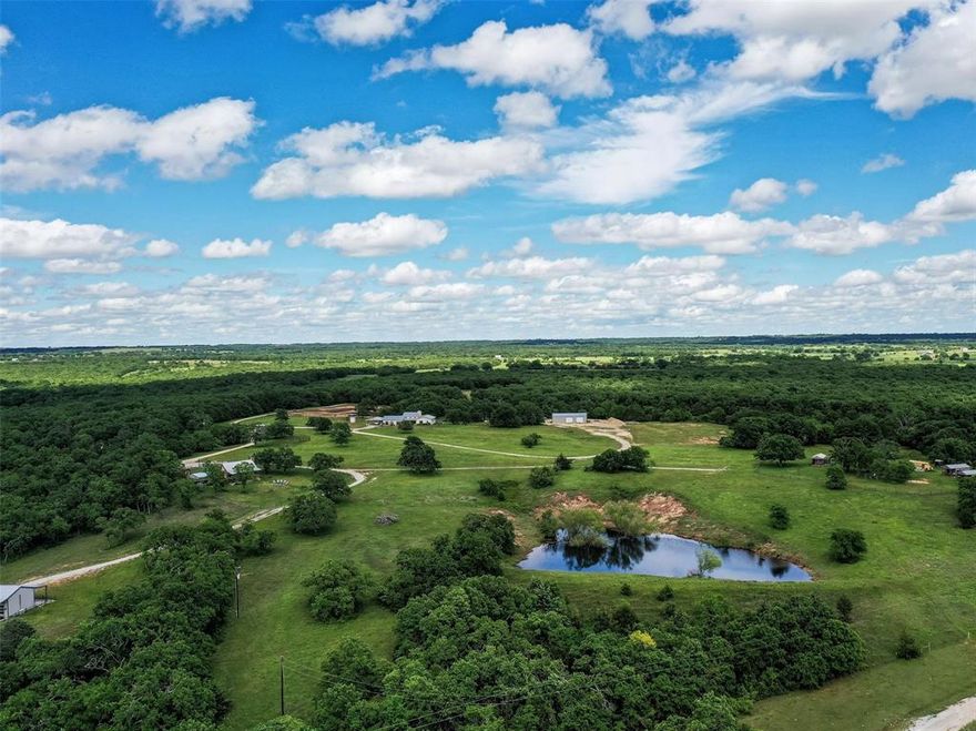 The Ponderosa Ranch – A stunning 157 acre property that offers the perfect blend of serenity and adventure. Nestled in the heart of nature, yet located just over an hour from DFW, this expansive ranch boasts of rolling hills and incredible ridge views and entails unique features that provide endless opportunities. Currently, the Ponderosa Ranch is a tranquil family residence that also functions as a business hosting events, retreats, classes and more. Upon arrival, you'll find a charming 2,394sf 3-bedroom, 2-bath modern farmhouse built with style and space for comfort. The open concept design has vaulted beamed ceilings, hand scraped wood flooring, stone fireplace, quartz countertops throughout and is filled with natural light. The property also includes ample storage and workspace, with a 20x30 workshop with electric and a 40x60 workshop for all your equipment and projects. The land itself is ag exempt, fully fenced, has pipe holding pens and is a paradise for outdoor enthusiasts. One of the two large stock tanks is stocked with bass and catfish providing recreational opportunities, while over 100 acres of oak, mesquite, and cedar trees create the ideal setting for hunting, hiking, trail riding and exploring. For guests or potential rental income, a beautifully designed authentic log cabin overlooks the hillside, offering cozy accommodations with breathtaking views. Also included, are four picturesque bunk houses, perfect for additional guests or a retreat, each containing their own bathroom and outdoor shower. For those seeking a space for creativity or business ventures, a unique 864sf studio, insulated and equipped with heat, ac, restrooms and glass roll-up doors, awaits with endless possibilities, whether it’s a yoga studio, venue for private parties, or a dream project. The Ponderosa Ranch offers not only the perfect retreat but also the opportunity to build a business, enjoy year-round recreation, or live a peaceful ranch life. Truly an incredible property!