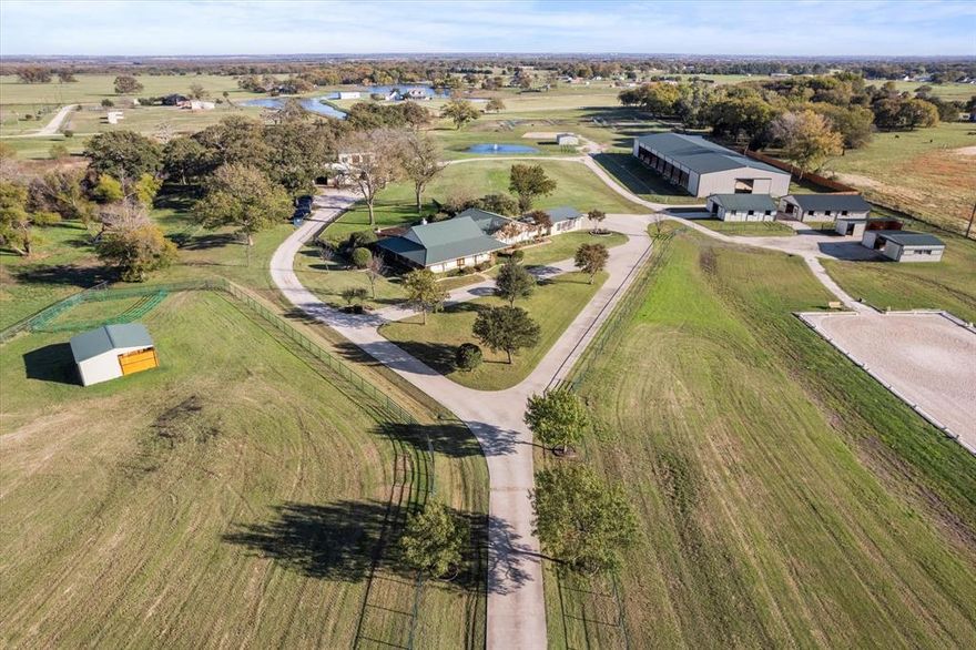 Your dream Ranch awaits on this picturesque almost 20 acre property in Pilot Point. This Exceptional Training Facility is thoughtfully designed to meet all of your needs starting with a 75 x 225 Covered Indoor Arena with Premier Equestrian Footing, seating area and LED lighting. In the front pasture you'll find a 70 x 200 Outdoor Arena with Premier Equestrian Footing with drainage system. Currently 22 Stalls in total, each barn hosting a Concrete Isle way. Facility is equipped with grooming and wash bays, tack room, 2 Loafing sheds, 70ft Square Lunging Pad, plus Guest Studio Apartment (Full Bath, Utility Room and Kitchenette). Six Pipe and No Climb Fence Turnouts – 2, 60 x 60 and 4, 60 x 100. Large work shop with two bays, tool area and plenty of storage, and RV hook-up. A charming wrap around porch invites you inside the main residence featuring a desirable, open-concept floor plan designed for entertaining. Gather  during the holiday season in the expansive living room highlighted by a cozy, wood burning stone fireplace. The well appointed kitchen is equipped with gorgeous cedar plank ceilings, stainless appliances, dual ovens, granite counter-tops, prep sink and Subzero refrigerator. Escape after a long day to the expansive primary bedroom complete with an ensuite bath and two walk-in closets. The whole family will love entertaining in the game or flex room. Lastly, make your way out to your serene backyard with a sparkling beach entry pool, covered patio and pergola, built-in Lynx grill and outdoor fireplace; you'll never want to leave!