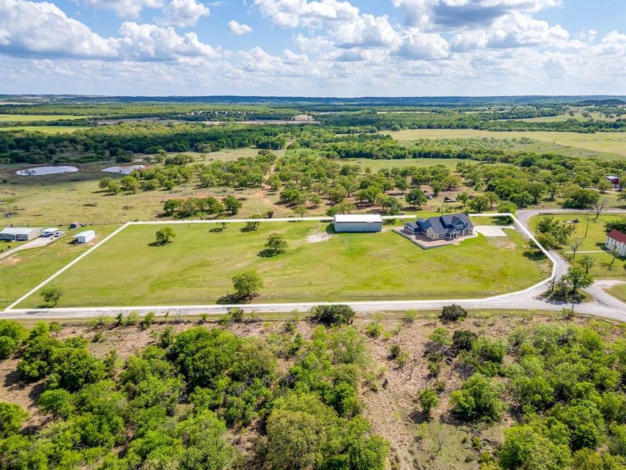 Welcome to a place where life slows down on this 4.8 acre estate in the highly sought-after Lipan ISD! This property has a standout feature of a 50x70 insulated shop equipped with air conditioning and heating, that is currently set up as an indoor sports barn. It offers a rare opportunity for sports training, private coaching lessons, local team practices and opens up the door (all three of them) for an income-producing potential in the growing Lipan youth sports industry. It has incredible built-in value from the potential commercial side. The home is a custom COUNTRY CHARMER with traditional farmhouse-feel of stonework, trending navy blue and white colors and INCREDIBLE VIEWS from the front porch!  A very functional and open concept layout, vaulted ceilings, picture windows with more views from the interior and a chef-approved kitchen! The kitchen has endless cabinets, a massive island with room for barstools and oversized butlers pantry with built-in wine storage.  A cozy primary suite, flex space with office, oversized laundry, mudroom and guest bedroom are all on the first floor. All remaining bedrooms are upstairs with roomy closets and jack and jill bathroom. Throughout the home has designer touches and an abundance of storage. Amazing property with more potential for horse arena and truly making it your own! Such a relaxing place to call home and experience this lifestyle. Don't miss out!