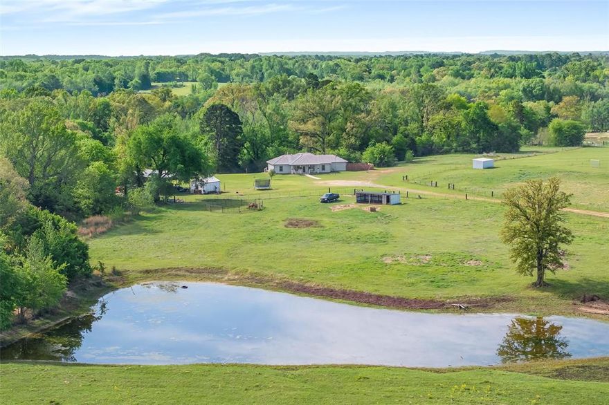 Country living on 23+ acres in East Texas. This 4BR-2BA home features an open-concept living and kitchen area with custom cabinetry & wood burning stove. Split bedroom floor plan with spacious primary suite & ensuite bath. Large secondary bedrooms, additional full bath, tankless hot water & generator. Ample storage with large laundry room and pantry. Exterior features include a covered front porch overlooking a pond & acreage, plus a covered back porch with ample space for outdoor living. Large covered carport provides room for vehicles, equipment & trailers; corral and storage building. Property includes approximately 23 acres with pond, hay meadow, and partial woods. Located minutes from downtown Winnsboro, with convenient access to Tyler, Longview, and the Dallas-Fort Worth area. Schedule showing to see all this property has to offer.