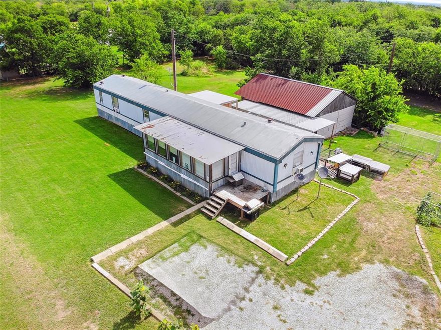 Tucked away in the heart of Pilot Point, this 1-acre property offers peaceful country living with open space, privacy, and endless potential. Just minutes from Hwy 377 and a short drive to I-35, this location provides the perfect balance of tranquility and convenience. The expansive lot features a double-wide mobile home, a large metal workshop with a red roof, and a fully fenced perimeter, ideal for those who desire space to grow, garden, store equipment, or simply enjoy wide open skies.

The mobile home includes an enclosed front porch, spacious layout, and multiple outbuildings, making it a great candidate for renovation or customization. Whether you're looking for a primary residence, weekend getaway, or investment opportunity, this property has excellent bones to build on. There’s a utility easement along the back of the property, ensuring no future development behind the lot and preserving your private views of nature. With mature trees, established fencing, and ample green space, this is a rare find with tremendous potential.