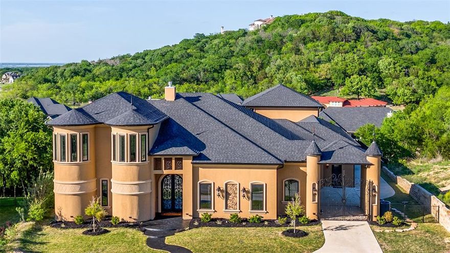Set within the rolling hills of Lakeridge, where Cedar Hill’s natural beauty meets some of North Texas’ most distinguished homes, this extraordinary custom estate offers privacy, scale & thoughtful design. Positioned to capture sweeping views of Joe Pool Lake & the distant Fort Worth skyline, the home is both a retreat and a striking vantage point. The architecture blends traditional forms with modern materials & meticulous detailing, the result of a hands-on design-build process. Inside, ceilings range from 12 feet in guest areas to over 22 feet in the main living spaces, filling the home with natural light & openness. At the center is a chef’s kitchen designed for everyday living & entertaining, featuring dual quartz islands, Thermador appliances, multiple ovens, warming drawer, wine refrigerator, ice maker, butler’s pantry, four sinks & two dishwashers. The adjoining living & dining areas flow seamlessly to the outdoors. The primary suite lives like a private residence, offering a sitting area with lake views, kitchenette, dual offices, and a spa-like bath with separate vanities, water closets & dual showers. A standout feature is the two-story boutique-style dressing room with custom cabinetry, integrated laundry, dry-cleaning station & a dramatic curved iron staircase leading to additional wardrobe & office spaces.
Two additional main-level bedrooms with ensuite baths provide comfort for guests. A dedicated theater room with soaring ceilings, immersive sound & fireplace creates a true cinematic experience. Outdoor living includes a 658-square-foot enclosed patio with full kitchen, fireplace & motorized screens for year-round use. A retaining wall & new fencing frame the property while preserving expansive lake views. A four-car garage offers extended depth, with unfinished space above ready for future living quarters. Located minutes from Joe Pool Lake, Cedar Hill State Park & Cedar Ridge Preserve, with easy access to Dallas, Fort Worth & both major airports.