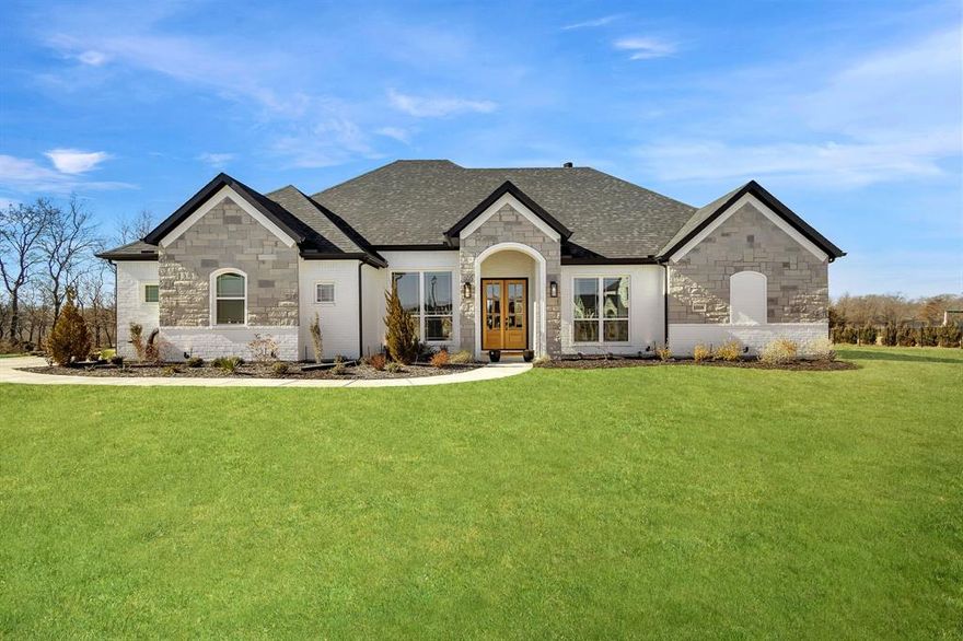 Stunning, contemporary one-story custom home on over one acre in Caddo Mills ISD. Appointed with every desired detail, this architectural beauty impresses the second one enters the majestic front doors. 4 bedrooms, 3 full baths; private bedroom and bath tucked away for guests. Kitchen w- huge island has Tier One black granite, under-counter lighting, 5-burner gas cooktop, pot filler, porcelain farm sink. Refrigerator stays! Living room w- majestic stone fireplace, raised hearth, gas-starter, sleek cabinetry and shelves. Big office w- coffered ceiling; can also be a flex room. Primary bedroom boasts ensuite bath w- a stylish soaking tub, built in dresser in closet, walk-in shower w- double shower heads, separate vanity. Very energy efficient w- tankless water heater, adjustable light levels on recessed lights, spray foam insulation in attic.  Covered back porch with fireplace, gas stub for grill. Very desired neighborhood-Minutes to I30, close to medical, shopping, entertainment.