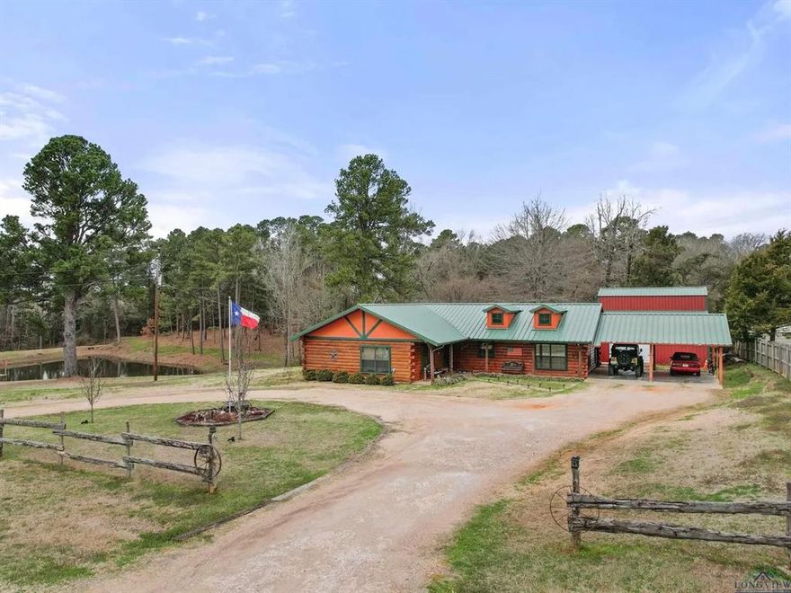 Welcome to the kind of East Texas property that instantly feels like a retreat, 5466 Glenwood Dr in Gilmer offers 5.15 acres of natural beauty, rustic charm, and room to breathe. The location is centrally located off Hwy 300 inbetween Gilmer and Longview. The driveway brings you home to a log-style residence with front-porch sweet tea vibes, surrounded by towering pines and peaceful views. On the exterior of this showstopper is a private pond, complete with a dock and covered sitting area—perfect for fishing, paddle-boat afternoons, or simply soaking up the sun while the trees reflect on the water. Inside, this 3 bedroom, 2 full bath home delivers that warm “cabin” feel buyers love—exposed beams, rich wood tones, character details, and an inviting split layout. The living space centers around a statement fireplace and comfortable gathering areas, while the kitchen offers plenty of storage and functionality for everyday living. As a bonus,  there’s the sunroom. A light-filled space with walls of windows to bring in natural light and showcase the peaceful setting. This flexible space makes a perfect spot for morning coffee, game nights, or winding down after a day on the pond. Need room for hobbies, tools, toys, or weekend projects? You’ll love the large shop garage 36X26 plus covered parking 20X24, giving you the freedom to work, store, and create without sacrificing space at the house. This home is part of the Lakewood HOA, additional HOA community information can be found at livingatlakewood.com