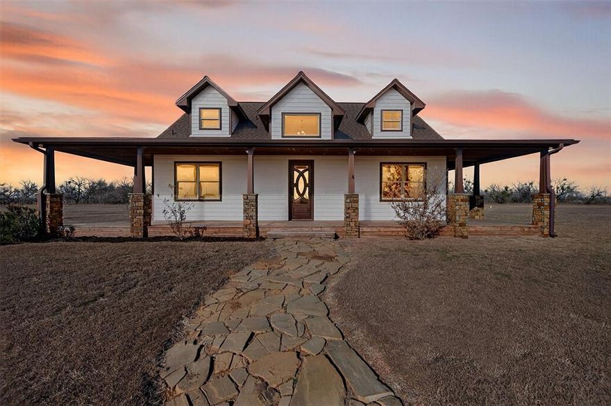 Experience refined Texas country living in this custom 3-bedroom, 2.5-bath home situated on just over 10 fully fenced acres, located outside the city limits of Graham, Texas. Thoughtfully designed with quality craftsmanship and rustic elegance, this property offers space, privacy, and functionality in a peaceful rural setting.

The exterior showcases a wraparound covered porch with stone columns, metal accents, and durable siding—perfect for enjoying wide-open views of the surrounding countryside. Inside, the main living areas feature stained concrete floors, an open-concept layout, and abundant natural light.

The kitchen is a standout, offering granite countertops, rich dark wood custom cabinetry, a large island with stone accents, and an oversized French-door refrigerator and freezer—ideal for entertaining or everyday living. The dining area flows seamlessly into the living space, creating a warm and inviting atmosphere.

The primary bedroom is located on the first floor and includes a spacious ensuite bath with dual vessel sinks, granite counters, a tiled walk-in shower, and a soaking tub. Additional bedrooms are located upstairs, connected by a loft-style landing that overlooks the main living area.

Outdoor living is equally impressive with a covered back patio kitchen, a small fenced backyard, and fully fenced acreage well-suited for animals, recreation, or future improvements. A deer feeder is already in place, adding to the property’s appeal for wildlife enthusiasts. The long private driveway enhances privacy while maintaining easy access to town. 

This home has been well maintained and offers a rare combination of modern comfort, quality construction, and usable land in Young County.