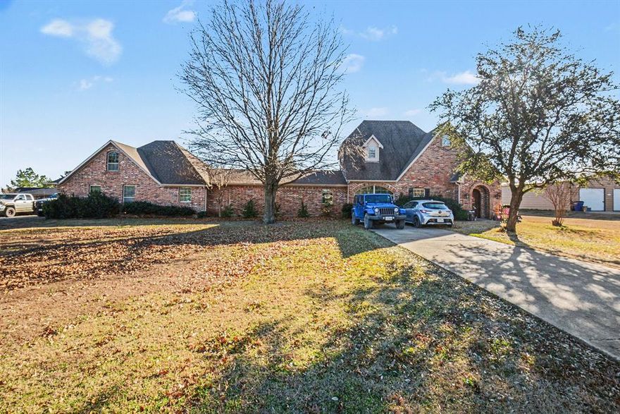 Motivated sellers relocating! This exceptional property offers over 2 acres of mature trees, complete privacy, and is surrounded by custom homes and equestrian estates. Elegant curved staircase, hardwood floors, and plantation shutters throughout. The main-level primary suite includes a sitting area and adjacent room ideal for a home office. A second family room opens to another spacious bedroom with en-suite bath. Upstairs features a convenient laundry room, game room, and large bedroom with built-in desk. The inviting dining room overlooks an expansive covered cedar porch. Outdoor amenities include a basketball court, 700 sq. ft. workshop, custom diving pool with cedar arbor, built-in outdoor kitchen (ready for Green Egg), additional storage building, water views, and a three-car garage. Garage includes Texas basement staircase leading to an 18x21 unfinished room, easily convertible to an additional bedroom. Highly regarded GISD schools. Surrounded by custom homes with no HOA.