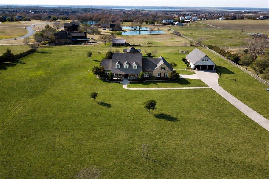 Set across more than four acres in one of Rockwall's most desirable locations, this exceptional property offers the rare ability to enjoy space, privacy, and flexibility without sacrificing comfort or convenience. From quiet mornings on the front porch to evenings entertaining outdoors or time spent in the workshop, the home supports a lifestyle that feels both elevated and intentional.
Meticulously maintained and thoughtfully improved, the residence features hardwood floors, abundant natural light, and living spaces that flow comfortably for everyday life and gatherings. A welcoming entry opens to a formal dining area, while a private office with custom built ins provides an ideal work from home setting. The main living area centers around a custom fireplace and opens seamlessly to a chef inspired kitchen with wood ceiling beams, quartz countertops, high end appliances, double ovens, custom cabinetry, and a copper farmhouse sink. A breakfast nook overlooks the expansive grounds.
The owner’s suite offers a peaceful retreat with a spa like bath and heated floors. Flexible spaces throughout the home allow for a media room, game room, additional bedroom, office, or second living area. A guest suite with its own entrance adds privacy and convenience for multi-generational living under one roof.
Outdoor living truly sets this property apart. A resort style pool, summer kitchen, and cabana with half bath create an inviting backdrop for entertaining and everyday enjoyment. The commercial grade workshop is a standout feature, offering substantial power on a separate electric meter, multiple bay doors, custom cabinetry, and ample concrete parking; ideal for hobbies, car collectors, business use, or storage. Miss those historically low interest rates? Fear Not, An assumable 2.25 percent loan may allow for lower monthly payments. This is a rare opportunity best experienced in person, schedule a private showing to fully appreciate all this property has to offer.