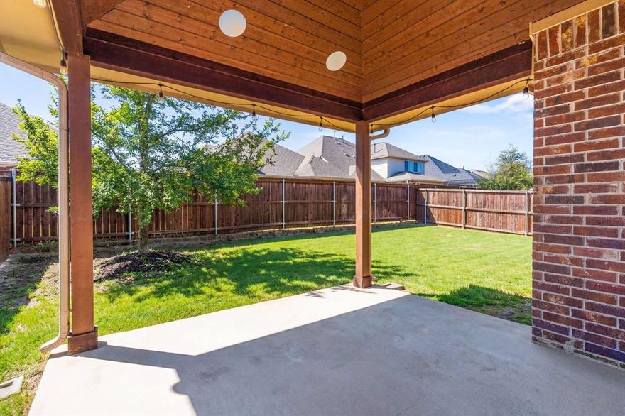 Exquisite single-story, energy-efficient home in the master-planned community of Trinity Falls in North McKinney. Lush trees and manicured landscaping frame the striking brick and stone façade, highlighted by a distinctive herringbone detail and elegant copper window awning, while an arched entry leads to the inviting brick front porch complete with a Ring doorbell and keyless entry. Inside, a dramatic circular foyer with tray ceiling sets the tone. Engineered wood floors flow throughout the main living areas. A versatile front bonus room—ideal as a home office, media, or game room—is wired with a Denon smart-home sound system for listening to music or watching the big game with surround sound. The private primary suite, accessed through French doors, features vaulted ceilings, four sunlit windows, custom built-in shelving, a sitting area, and two generous walk-in closets. End a long day in the spa-inspired bathroom, which offers dual sinks with granite countertops, a soaking tub beneath a large window, a walk-in tile shower with body spray, and a private water closet. Enjoy cooking and baking in the eat-in kitchen that boasts white cabinetry with deep drawers for pots and pans, granite countertops, tile backsplash, walk-in pantry, and an island with undermount dual sink and upgraded pull-down faucet. Host dinner parties or family meals in the light and bright dining area and gather your loved ones in the cozy living room, anchored by a gas fireplace and vaulted ceilings, with patio access for seamless indoor-outdoor living. The covered patio is an entertainer’s dream, showcasing a vaulted pine ceiling with fan, in-ceiling speakers, and gas stub in place for outdoor grilling. A spacious backyard with grassy play area completes the setting. Community amenities include pools, ponds, dog park, pickleball, playgrounds, Frazier Elementary, and easy access to Hwy 75.