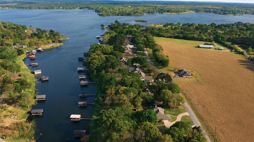 Located on a deep water cove just off open water, this exceptional lakefront property offers a beautiful , tranquil setting with mature trees, a landscaped yard, and refreshing lake breezes.  The home features outstanding drive-up appeal with a circle drive and abundant parking for guests.  Inside, the open-concept design showcases high ceilings and a striking stone fireplace, complemented by large picture windows with transom windows above that fill the space with natural light and capture serene lake views.   Glass doors lead to a covered porch, creating a seamless connection between indoor and outdoor living.  The well-appointed kitchen features granite countertops, abundant cabinetry, and a convenient serving bar.  The dining area is surrounded by three walls of windows, offering spectacular lake views while you dine.  The primary suite is a peaceful retreat with raised ceilings, large windows, and a garden door leading outside.  The spacious bath includes dual vanities, a soaking tub, and a walk-in shower.  The outdoor spaces are truly special, designed to fully enjoy the beauty of the lake.  A large covered porch overlooks the water, while a stunning flagstone patio with a fire pit and built-in stone bench seating creates the perfect setting for relaxing evenings.  A pea gravel pathway leads to a secondary stone patio, providing an additional private outdoor gathering area.  The private boat dock features a sundeck ideal for fishing, swimming, or simply enjoying the clear waters of the lake, all set along 116 feet of beautiful shoreline.