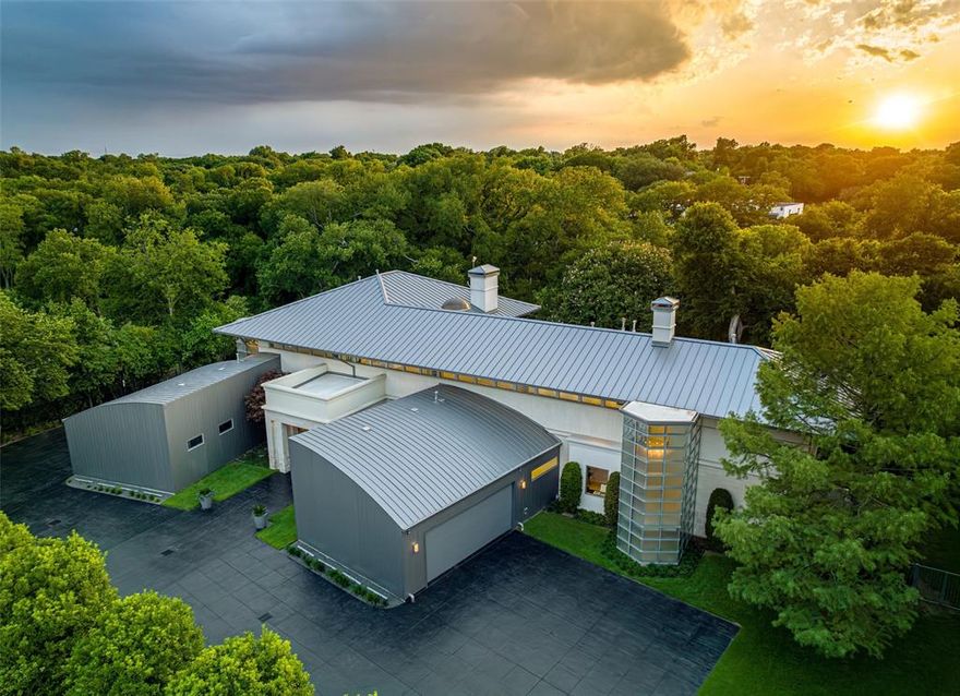 This North Dallas contemporary home designed by architect Charles Fisk is brimming with special details. The 6,728 sqft residence boasts 4 beds, 4.1 baths, a game room, a media room, multiple balconies, and a meticulously landscaped 1.278-acre lot. The first level’s unique architectural dining room with a circular mahogany exterior and the spacious living room with a striking fireplace offers a grand place to entertain. The sleek kitchen features black granite counters, maple cabinetry, and limestone floors. Upstairs the primary is a serene oasis with treetop views, a covered balcony, and light-filled bathroom with heated tile floors. In the backyard, find a large patio with a built-in grill and fire pit. The sparkling pool features a hot tub and waterfall. In addition to the 4 garage spots, a paving unit with special irrigation that is found under the grass creates more guest parking. The architecture blends seamlessly with the meticulous grounds, creating an entertainer’s dream.