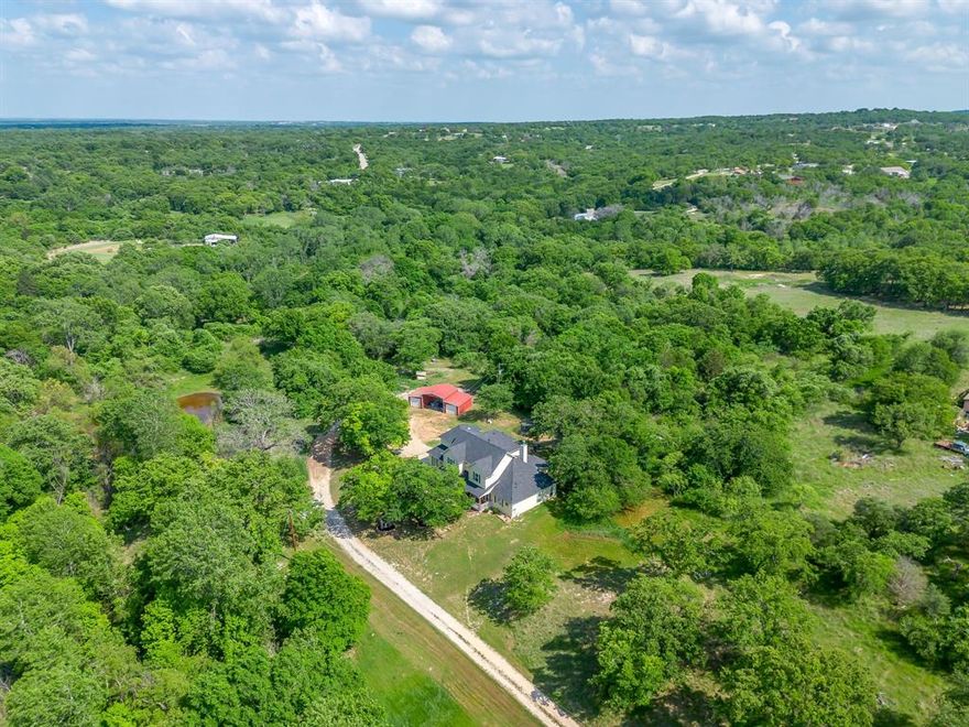 Picture perfect country charm found here in the quintessential farmhouse with front and back porches, a knock-out floor plan, thoughtful upgrades - and all on 6+ acres of gorgeous land just 15 minutes away from Springtown. Whole-house foam insulation, a 2 year old HVAC, a Class III hail resistant roof installed 2025, central vacuum, reverse osmosis and water softener, and Terminix prevention perimeter tubes...so much value in the thoughtful upgrades made to this custom built home. The inviting interior manages to be hard working and beautiful: abundant built-ins in the dedicated office and also flanking the wood burning fireplace with big hearth. Kitchen checks all the boxes with gas cooktop, big island, double ovens, stainless steel bib sink and a coffee bar. The primary suite is serene and even features laundry hookups in the closet. The pantry is over-the-top huge. And upstairs you'll find three huge bedrooms, giant closets, and smartly laid out bathrooms - all with dual sinks and separate water closets and showers. So much storage throughout - including the massive upstairs laundry room. Outdoors, adventure and projects await with a seasonal creek, pond, mature trees, and room for gardening, animals, and more. Make use of the red barn and the RV pad with hookups. This is where you have the freedom to dream and the room to play!