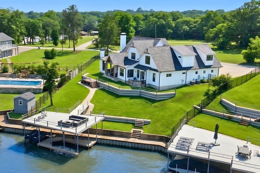 Just one hour from Dallas, 205 Oak Creek Drive isn’t just a lake house—it’s a destination. Perched above the shoreline in the heart of Cedar Creek Lake, this custom modern farmhouse delivers sweeping water views, refined indoor-outdoor living, and spacious design ideal for gathering friends and family year-round. Inside, the open-concept layout centers around a vaulted great room with warm wood beams, shiplap walls, and a stone fireplace. Expansive windows and French doors flood the space with natural light and stunning lake views. The designer kitchen boasts quartz countertops, a large island, and premium finishes—perfect for morning coffee, holiday spreads, or casual dinners for twelve. The flexible layout includes a main-floor study (or guest suite) with a full bath, plus a secluded primary suite with private patio access to enjoy sunrise on the water. Upstairs, two guest bedrooms with en-suite baths provide comfort and privacy, while the massive rec wing includes a bunk nook, full bath, game room, and private bedroom—ideal for kids, teens, or extended guests. Outside, a wraparound covered porch with porch swings, an outdoor fireplace, and built-in grill offers the ultimate entertaining space—perfect for hosting Thanksgiving by the fire or watching football with a lake breeze. The fenced yard leads to a private boathouse with a 25-ft boat slip, two jet ski lifts, and a party deck with open water views. Located in the friendly Arnold Hills community, 205 Oak Creek is perfect as a full-time home, holiday hub, or weekend retreat—just a short drive from the city, but a world away in experience.