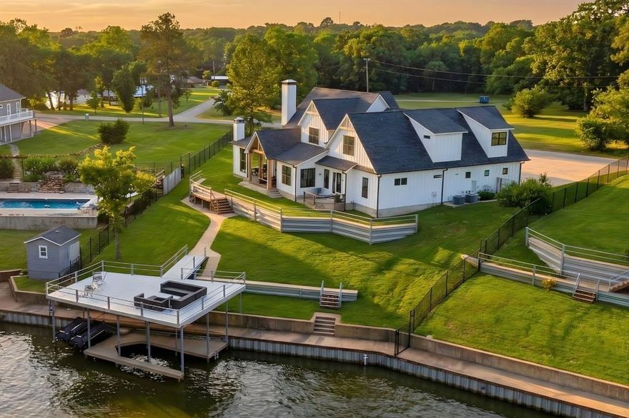 Just one hour from Dallas, 205 Oak Creek Drive isn’t just a lake house—it’s a destination. Perched above the shoreline in the heart of Cedar Creek Lake, this custom modern farmhouse delivers sweeping water views, refined indoor-outdoor living, and spacious design ideal for gathering friends and family year-round. Inside, the open-concept layout centers around a vaulted great room with warm wood beams, shiplap walls, and a stone fireplace. Expansive windows and French doors flood the space with natural light and stunning lake views. The designer kitchen boasts quartz countertops, a large island, and premium finishes—perfect for morning coffee, holiday spreads, or casual dinners for twelve. The flexible layout includes a main-floor study (or guest suite) with a full bath, plus a secluded primary suite with private patio access to enjoy sunrise on the water. Upstairs, two guest bedrooms with en-suite baths provide comfort and privacy, while the massive rec wing includes a bunk nook, full bath, game room, and private bedroom—ideal for kids, teens, or extended guests. Outside, a wraparound covered porch with porch swings, an outdoor fireplace, and built-in grill offers the ultimate entertaining space—perfect for hosting Thanksgiving by the fire or watching football with a lake breeze. The fenced yard leads to a private boathouse with a 25-ft boat slip, two jet ski lifts, and a party deck with open water views. Located in the friendly Arnold Hills community, 205 Oak Creek is perfect as a full-time home, holiday hub, or weekend retreat—just a short drive from the city, but a world away in experience.