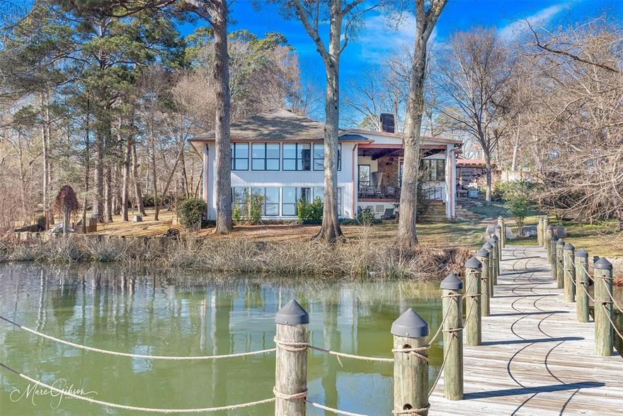Tucked away on 2 wooded acres with 165 feet of protected Cross Lake shoreline, this one-of-a-kind 5,313 SF lakefront retreat blends rich Louisiana heritage with refined modern luxury. Located at 2949 Moss Point Drive outside of Shreveport City Limits, the property was originally discovered by hunters in 1948 and named Willow Cove for the abundance of willow trees that once lined its peaceful cove. What began as a humble fishing cabin has evolved through thoughtful expansions and a major renovations into a 4-bedroom, 4.5-bath architectural showpiece filled with rare reclaimed materials—150-year-old antique wood beams, sinker pine floors recovered from the Ouachita River, antique plantation balusters and handcrafted details throughout. Designed for both grand entertaining and relaxed lake living, the open floor plan showcases sweeping water views, a dramatic living area with tiered gathering steps and a wood-burning fireplace, formal and casual dining spaces, and a true Chef’s kitchen featuring custom cabinetry, a 12-foot pecky cypress island with beautiful Bordeaux granite, hand-forged copper sinks, wet bar, pot filler, and premium appliances by Wolf, Sub-Zero and Miele. Multiple guest suites—including a private 1000SF downstairs living quarters with kitchenette and separate HVAC—offer exceptional flexibility, while the serene primary suite opens to a glass-wrapped sun porch overlooking the lake. Outdoor living shines with covered decks, an outdoor cooking area, a dock in a calm cove ideal for swimming and wildlife watching, greenhouse, lake-fed irrigation, mature native trees, and recent upgrades including new cedar garage doors and fencing. With maintained systems including 3 HVAC systems, a whole-home Kohler generator, water well, treatment systems and unmatched privacy just minutes from town, this storied property delivers peaceful waterfront luxury in one of Cross Lake’s most distinctive settings. Schedule a private showing. See attached list of features.